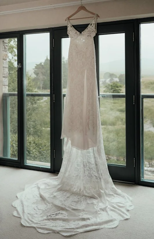 wedding dress hanging up in front of a countryside view through windows