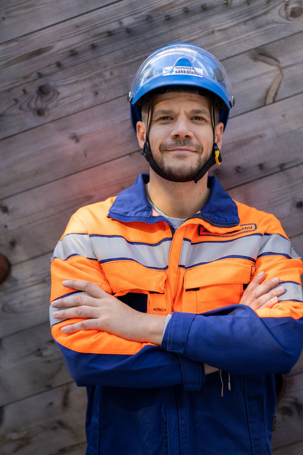 Työvaatteisiin pukeutunut henkilö poseeraa seinää vasten.