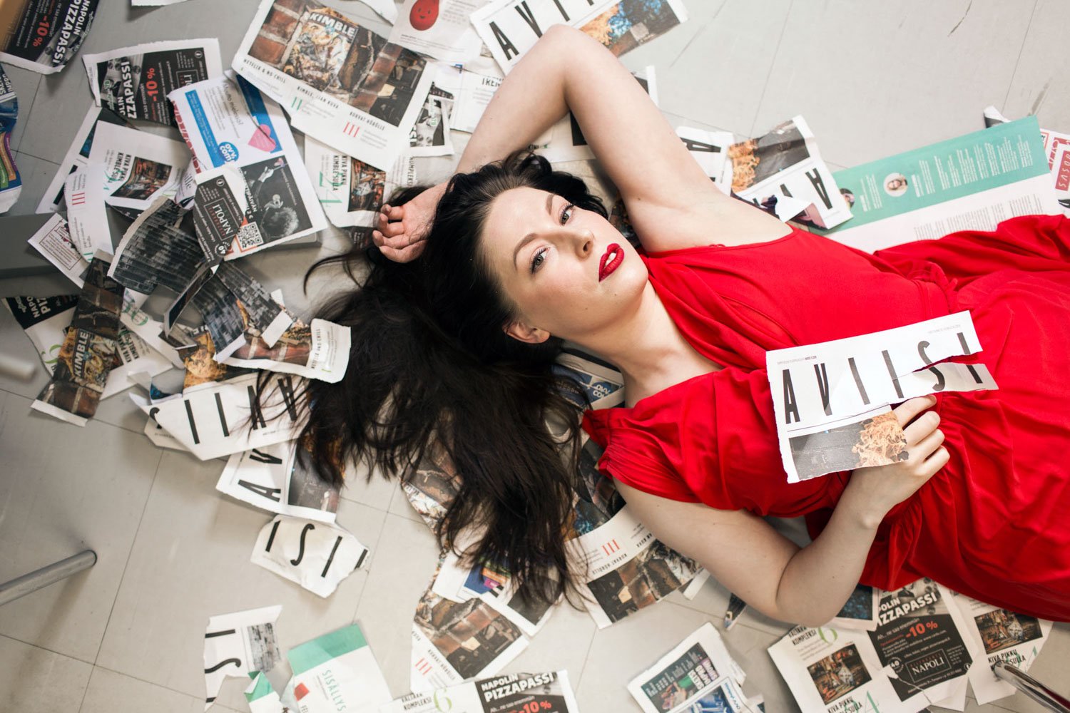 Toimittaja Tuija Siltamäki makaa selällään lattialla revittyjen Aviisi-lehtien päällä.