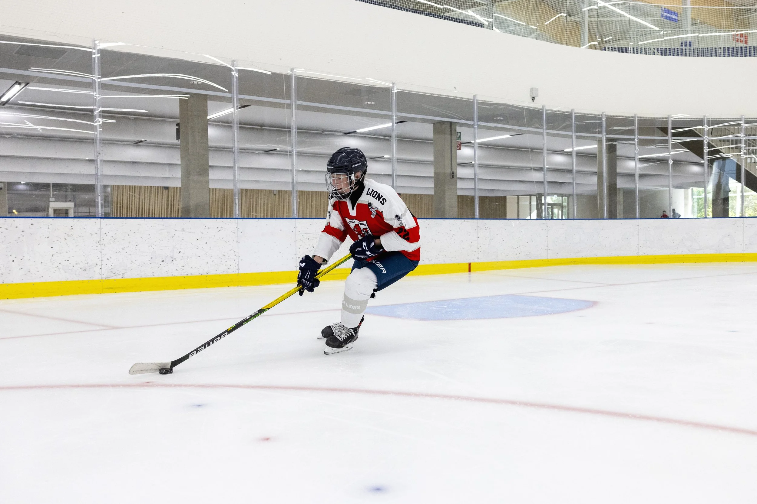 Een kind in een ijsbaan die hockey speelt, gekleed in een hockeyoutfit en met een helm en stick.