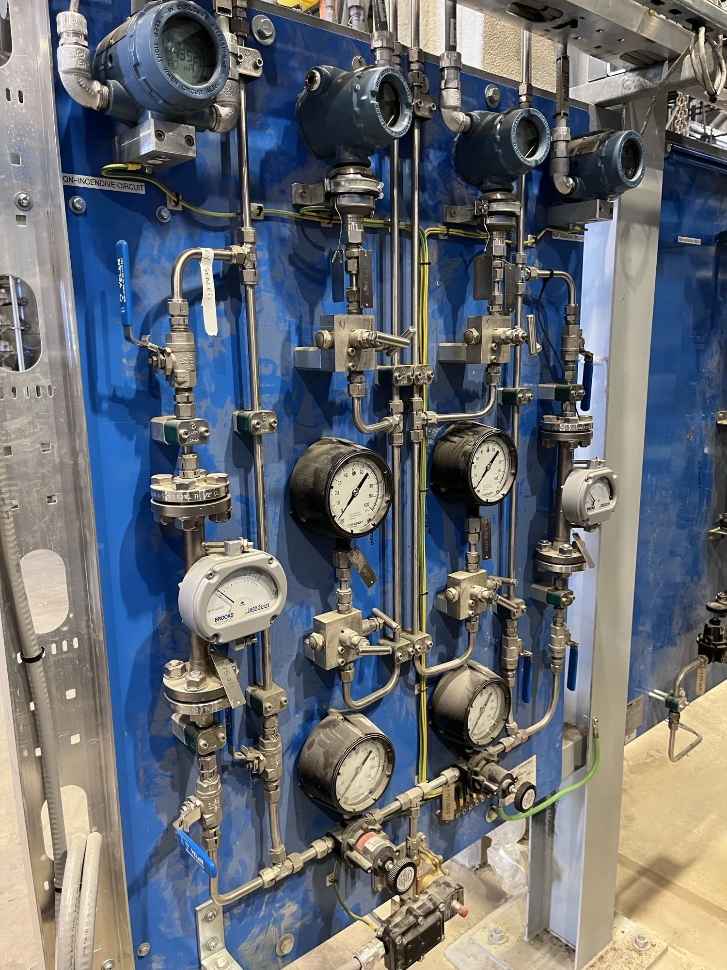 Industrial control panel with gauges, pipes, valves, and meters mounted on a blue panel.