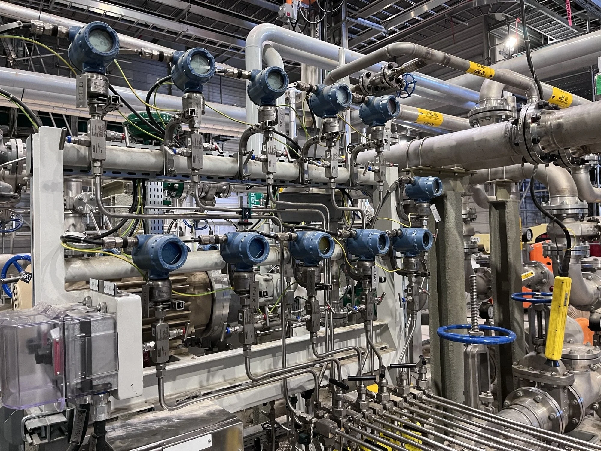 Industrial piping system with blue valves, pressure gauges, wires, and metal pipes.