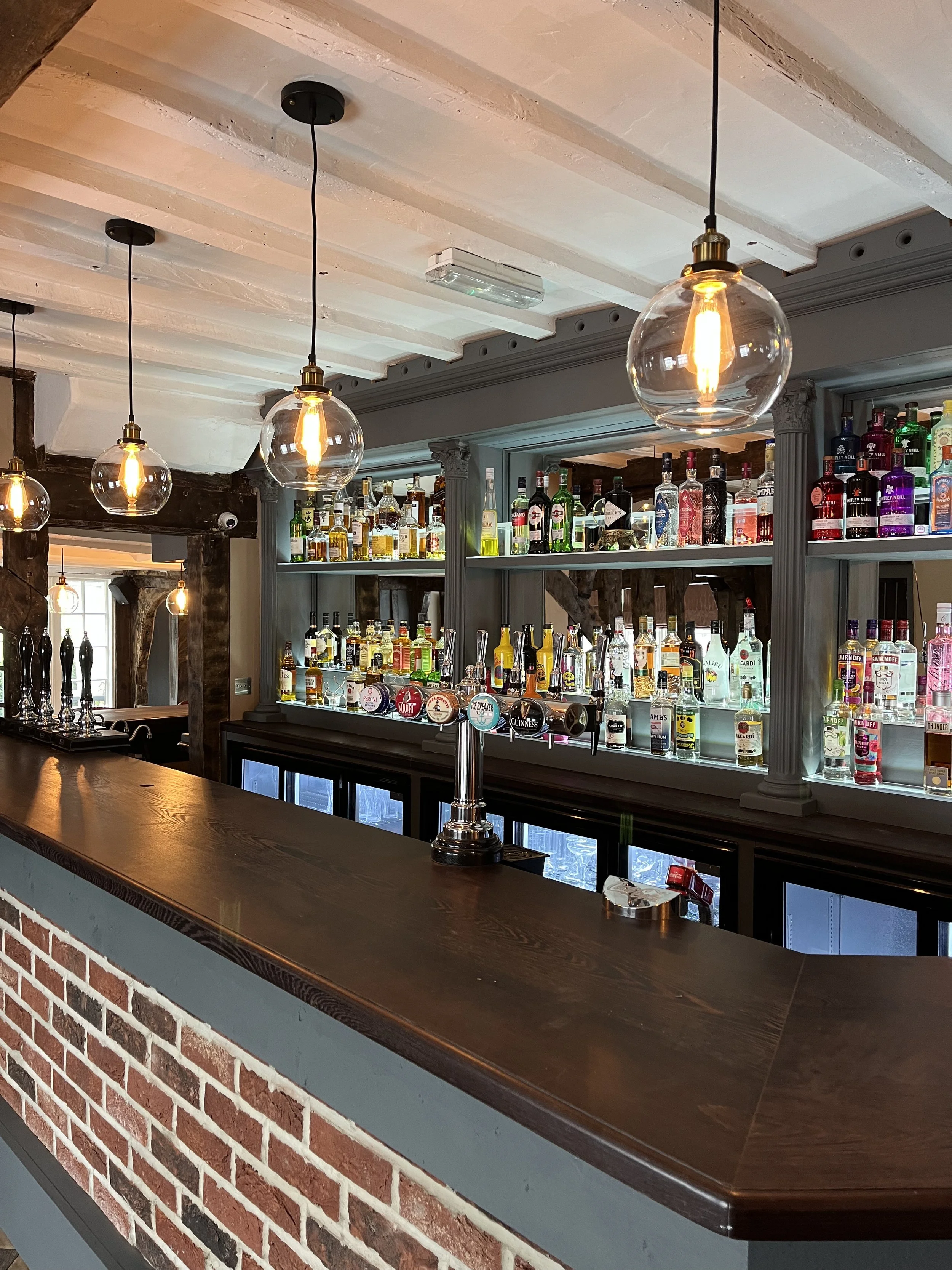Interior of a bar with hanging globe lights, a wooden counter, and shelves stocked with liquor bottles.