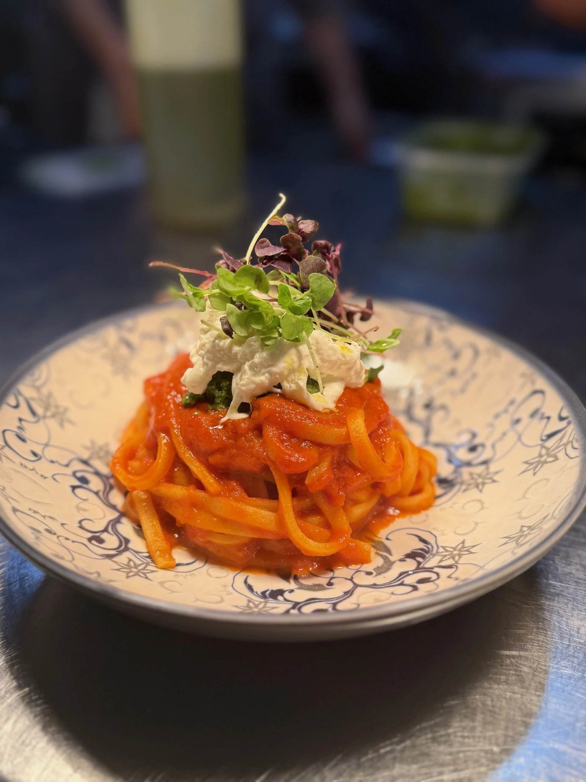 Plate of spaghetti with tomato sauce, topped with cheese, microgreens, and herbs, served on a decorative white plate.