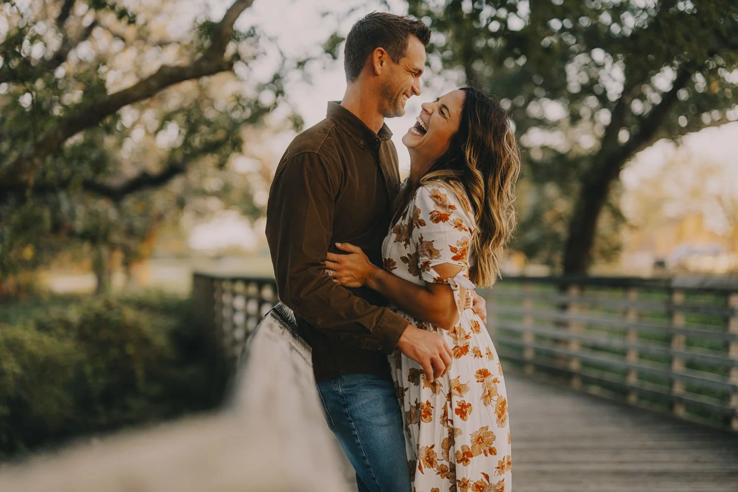 A happy couple sharing a joyful moment outdoors near a fence with trees in the background.