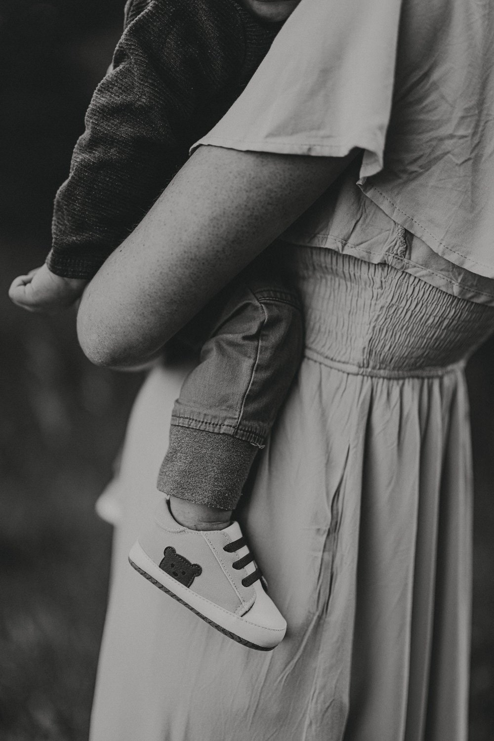 A person holding a child by the leg, with the child wearing a sneaker with a teddy bear face on it.