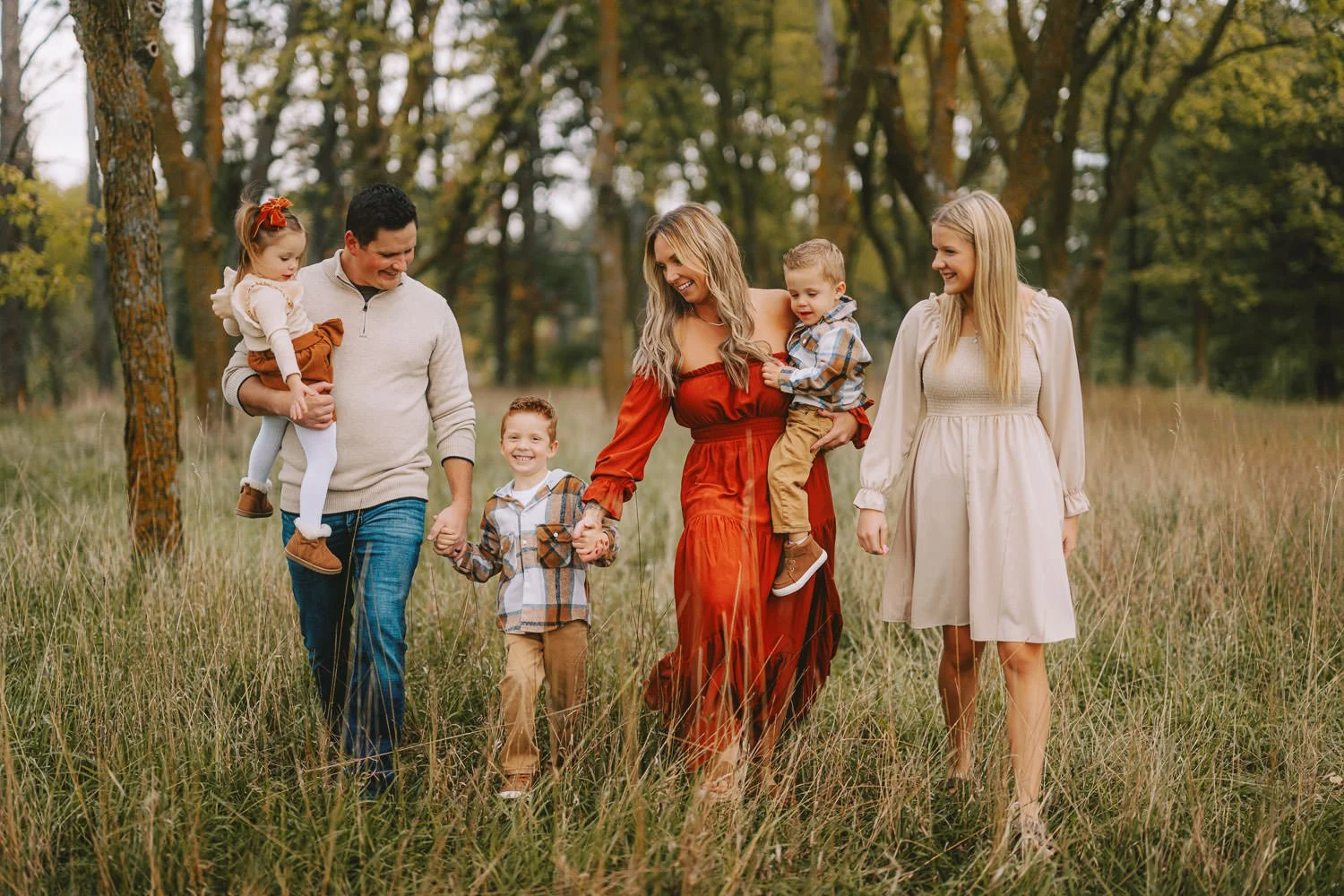 Family walking through a grassy field in autumn, holding hands and smiling