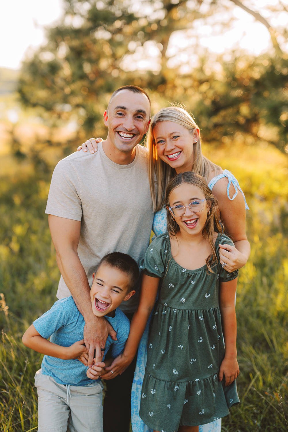 A happy family of five standing outdoors in a park during sunset, smiling and enjoying each other's company.