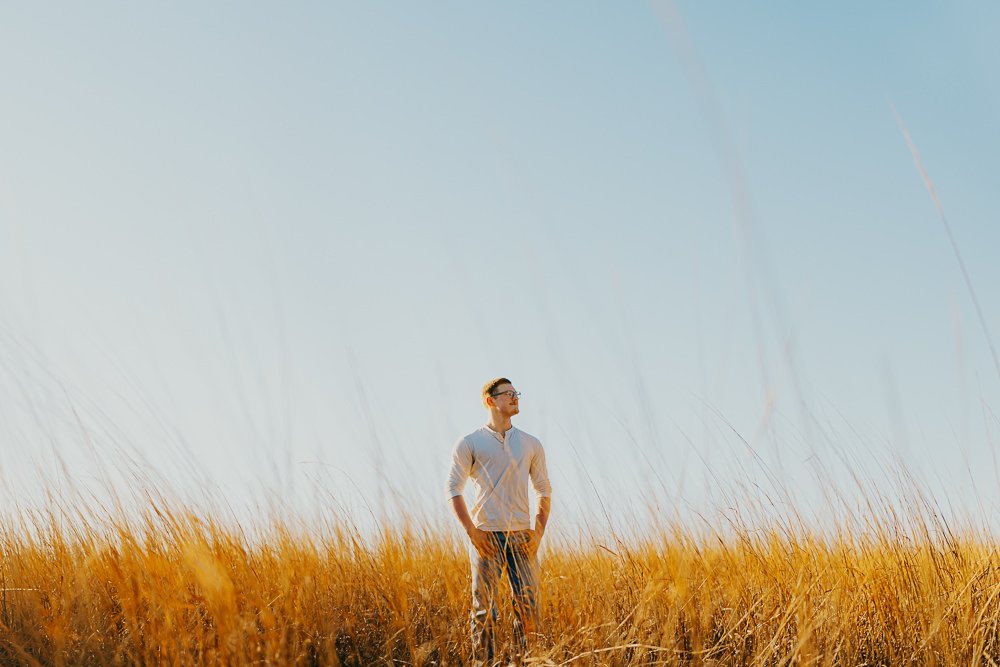 A man standing in a golden field of tall grass under a clear blue sky.