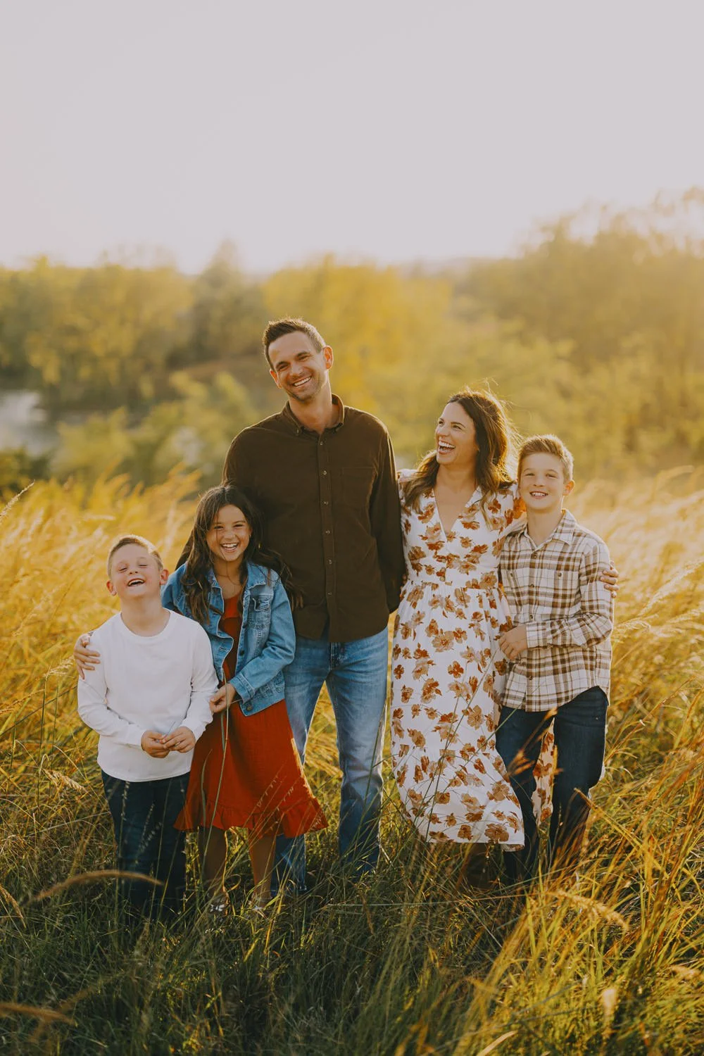 A happy family of six outdoors in a golden field during sunset, smiling and laughing.