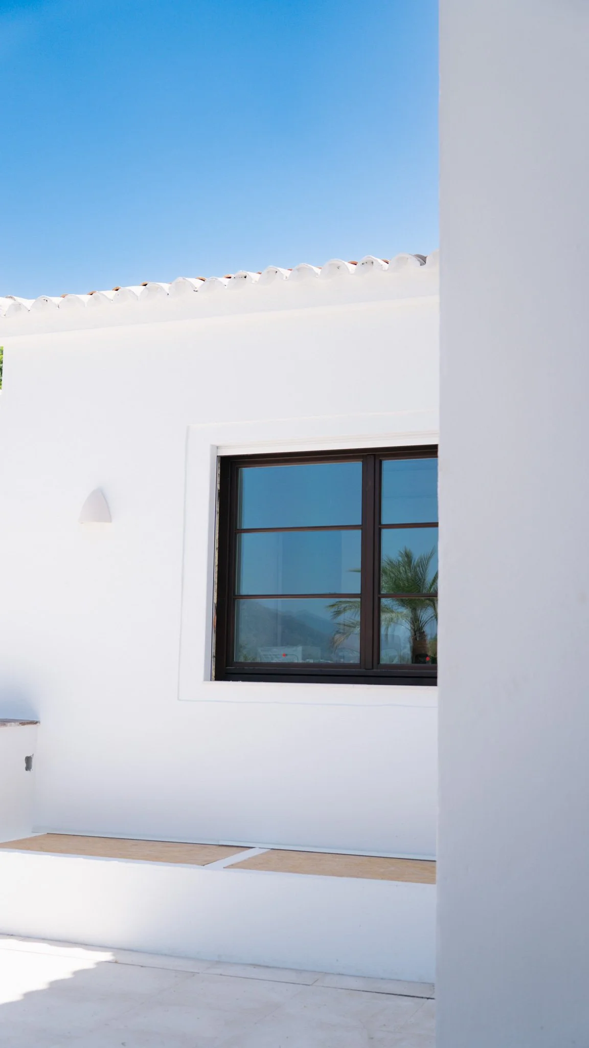 Bright living room with white and natural wood decor, large windows, a white sofa with throw pillows, a coffee table, and a dining area with a white table and chairs.