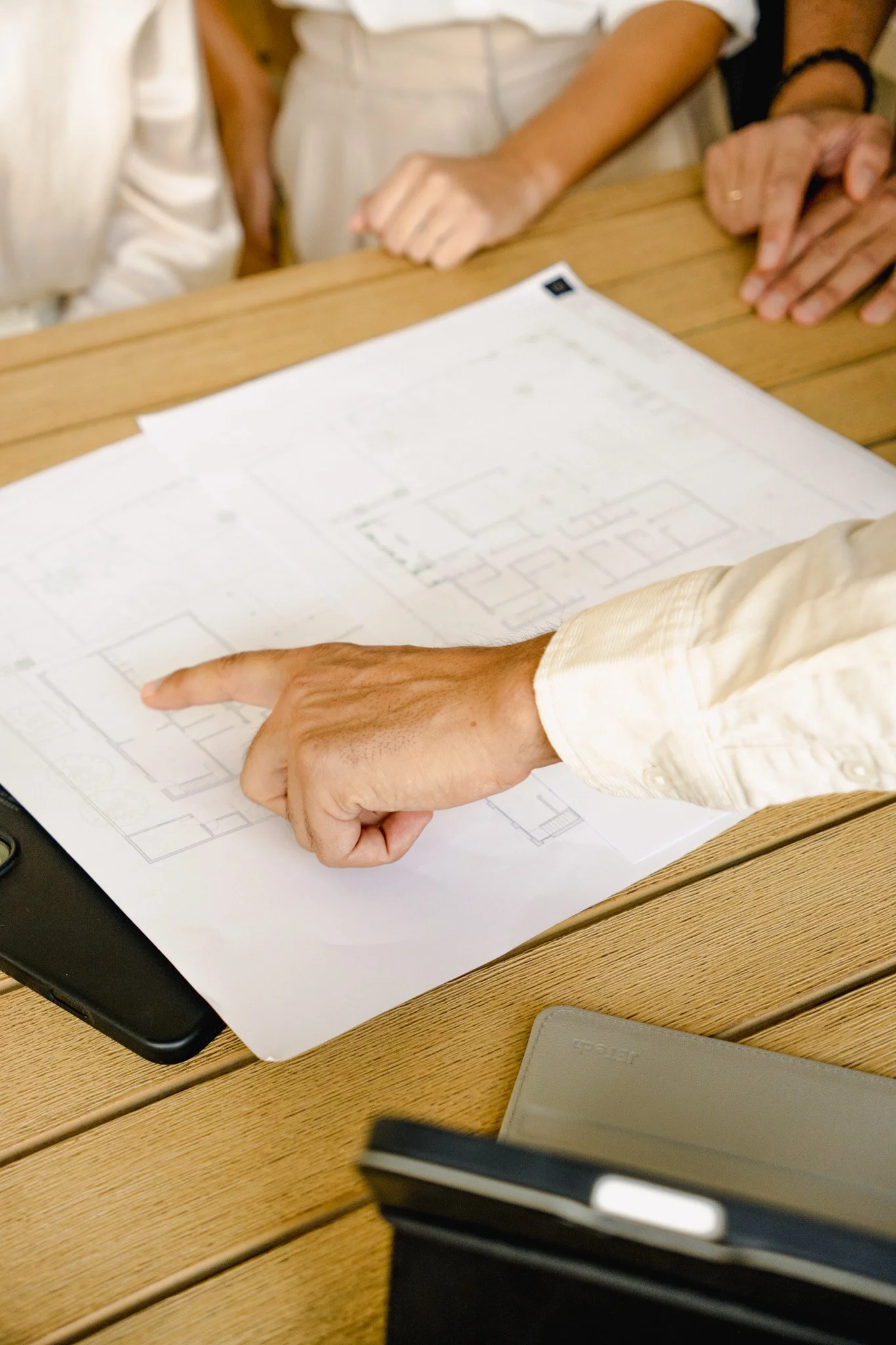 Person in denim jacket pointing at a blueprint of a building on a table surrounded by other architectural plans.