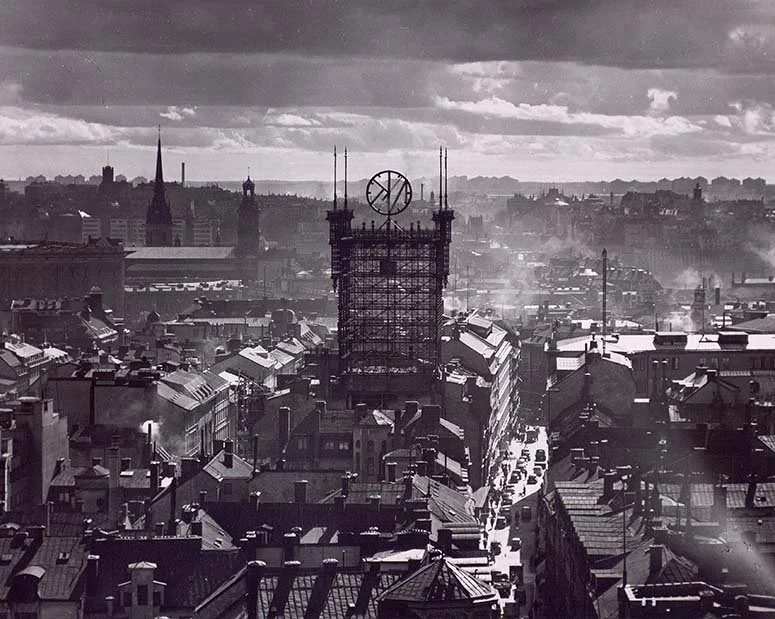 Black and white aerial photo of an ornate metal tower with a revolving clock mounted on the top