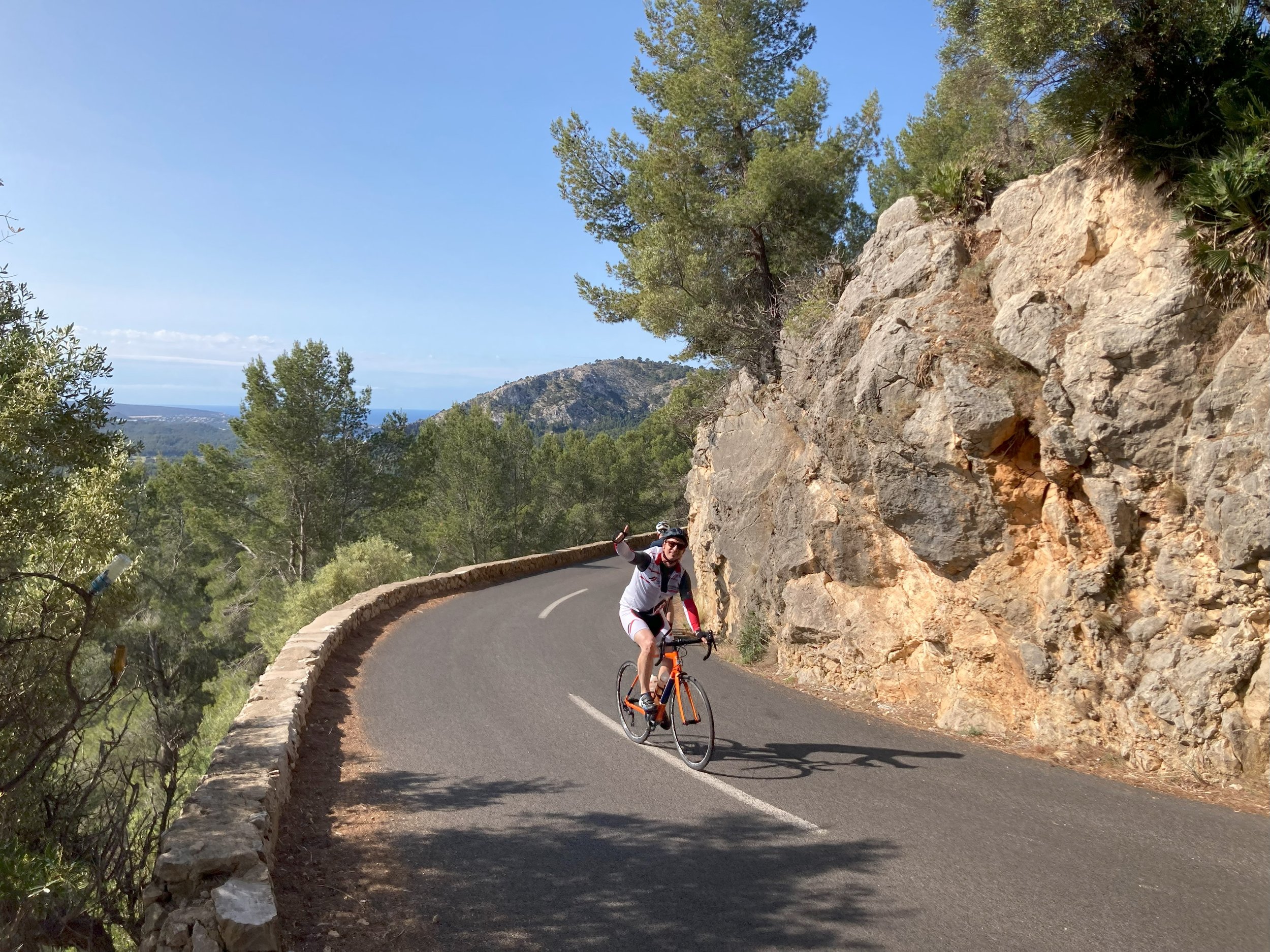 Cykelrytter på orange cykel på vej op af bjergstigning på Mallorca på netværksrejse arrangeret af Groossartig.