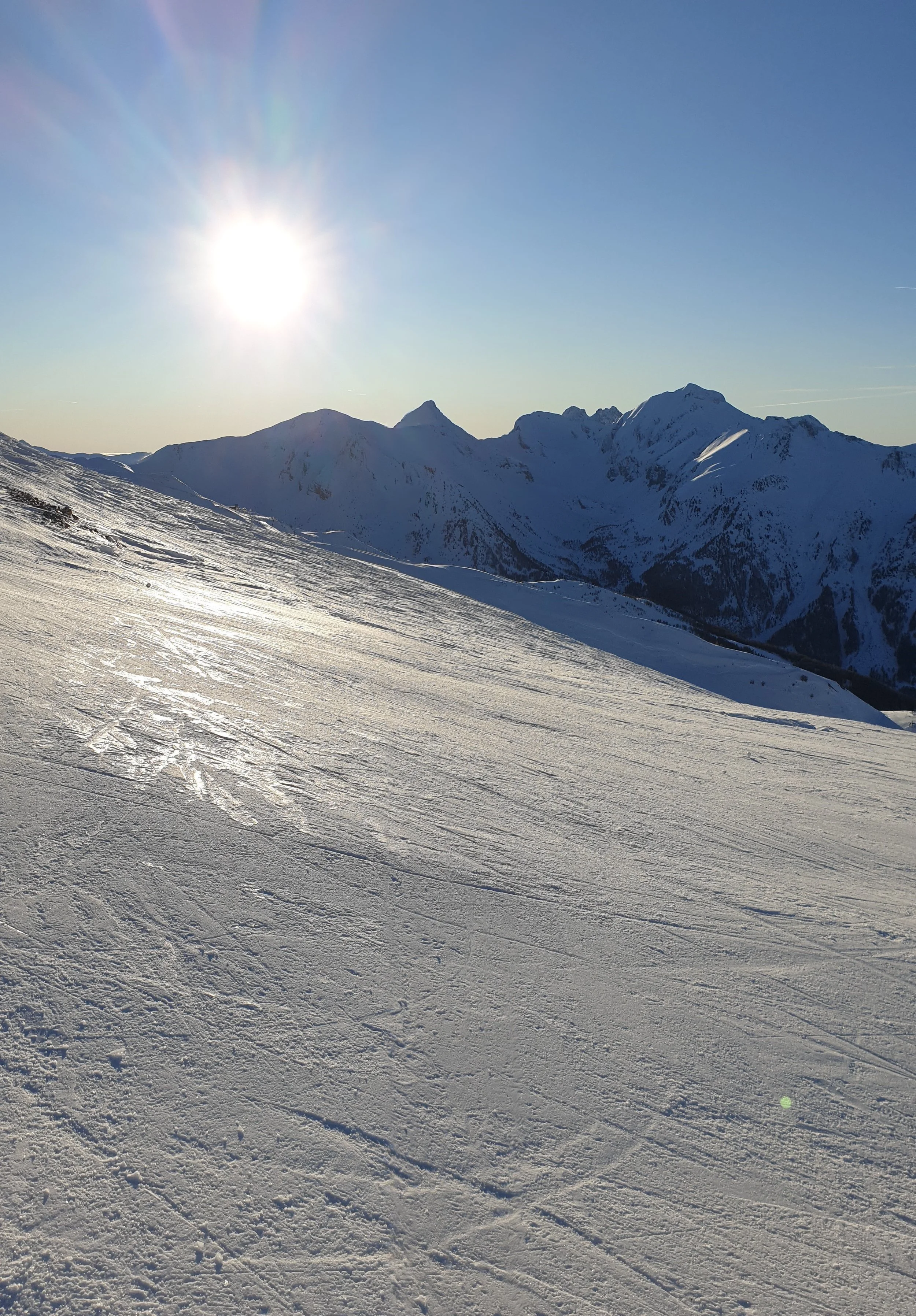 Skibakke med skispor i høj solskin og blå himmel.