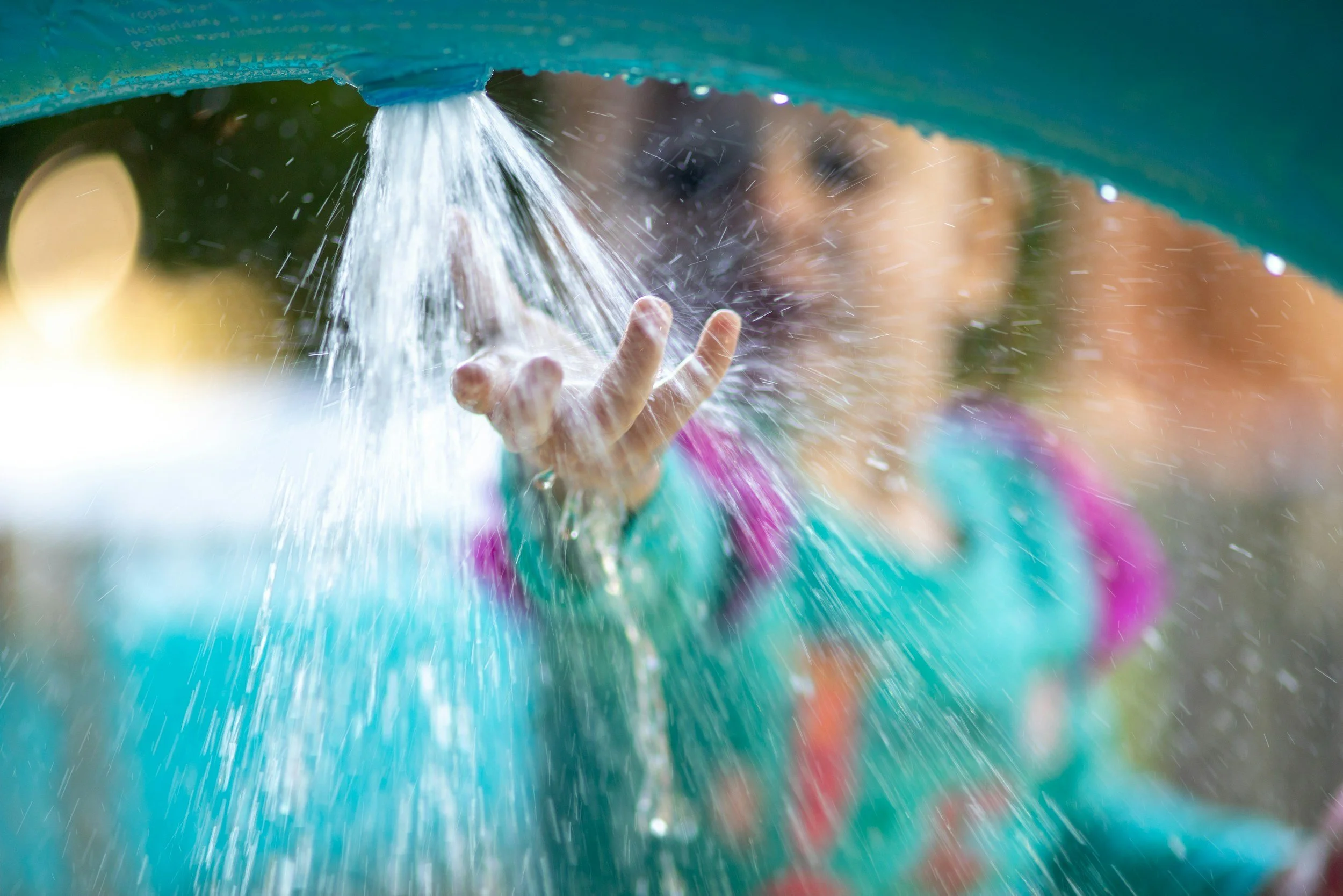 A young girls in a turquoise swimming suit holds her hand under running water.