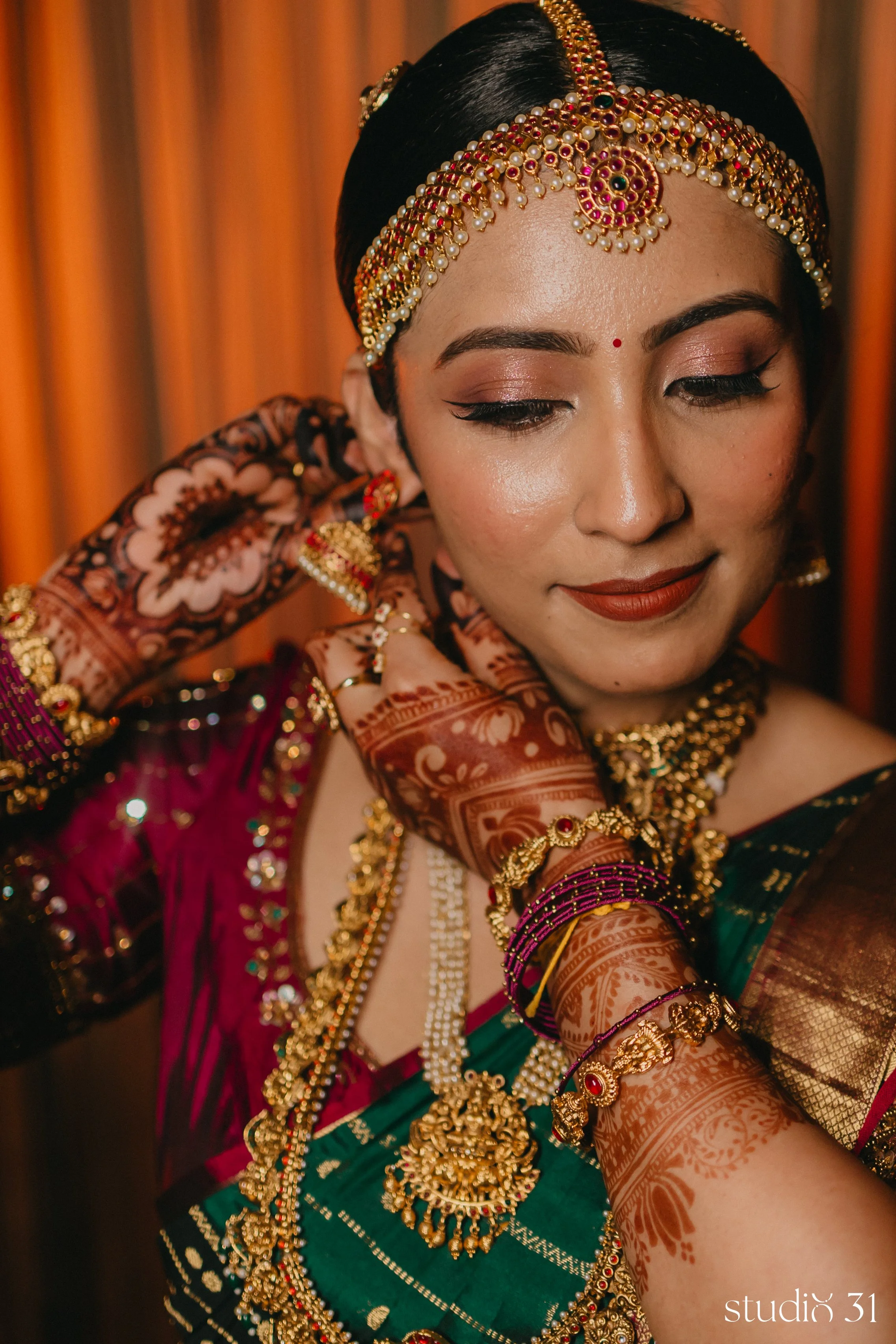 Close-up of a woman in traditional Indian attire, wearing colorful jewelry and henna on her hands, with a warm background.