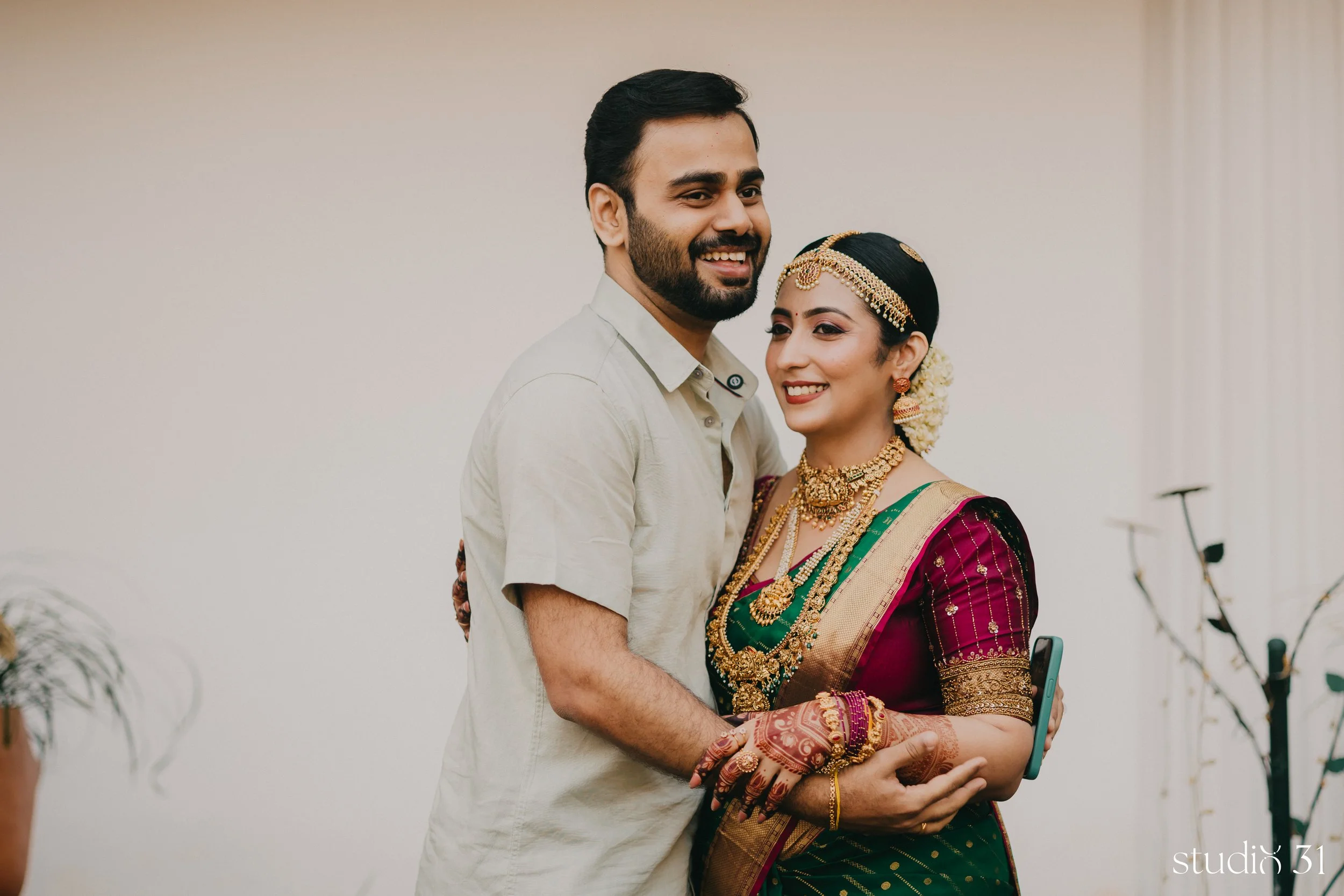 A person in traditional Indian attire, heavily decorated with jewelry, being embraced by a man in a casual shirt, both smiling.