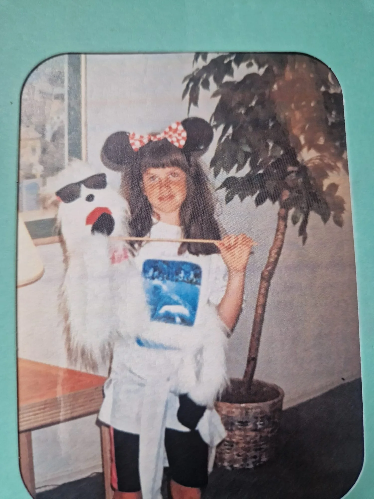 A young girl with long dark hair and bangs stands at the center of the frame. She is wearing a white t-shirt featuring a prominent blue graphic of a whale or marine animal, which aligns with her lifelong passion for the natural world.