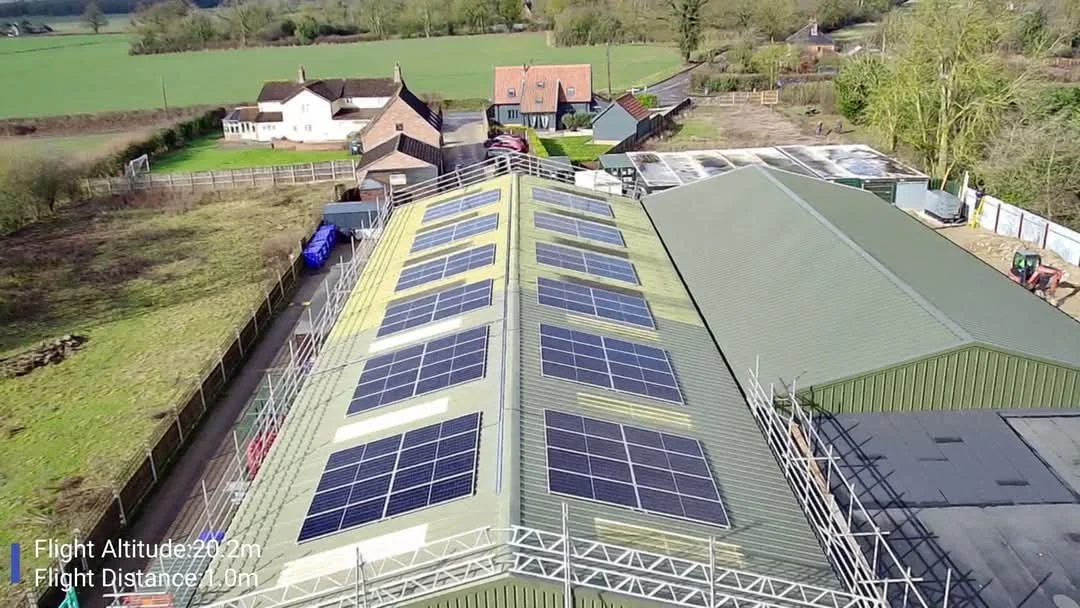 An aerial view of a building with solar panels on its roof, surrounded by residential houses and green fields.