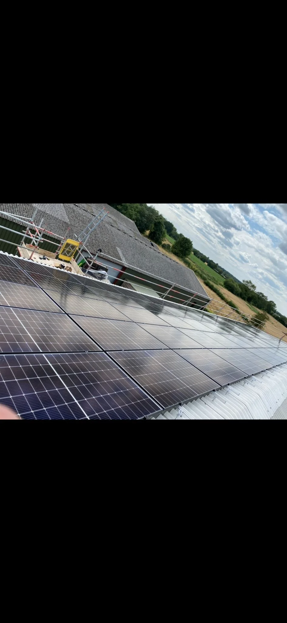Photograph of solar panels installed on a roof with a rural landscape in the background under a partly cloudy sky.