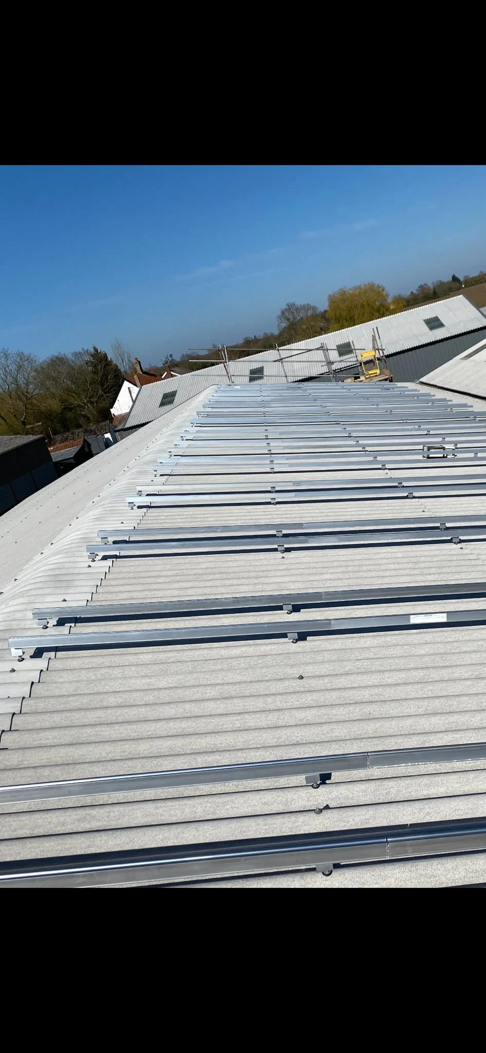 View of a metal roofing construction site, showing partially installed white metal panels and metal support beams under a clear blue sky.