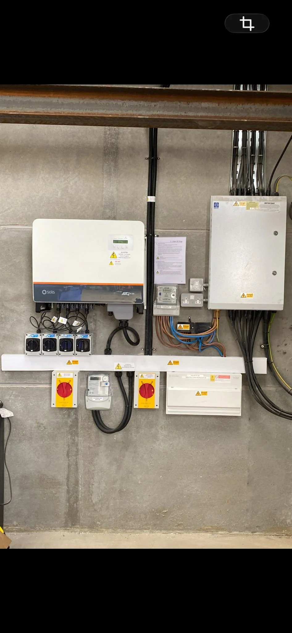Electrical panel with meters, switches, and wiring mounted on a concrete wall.