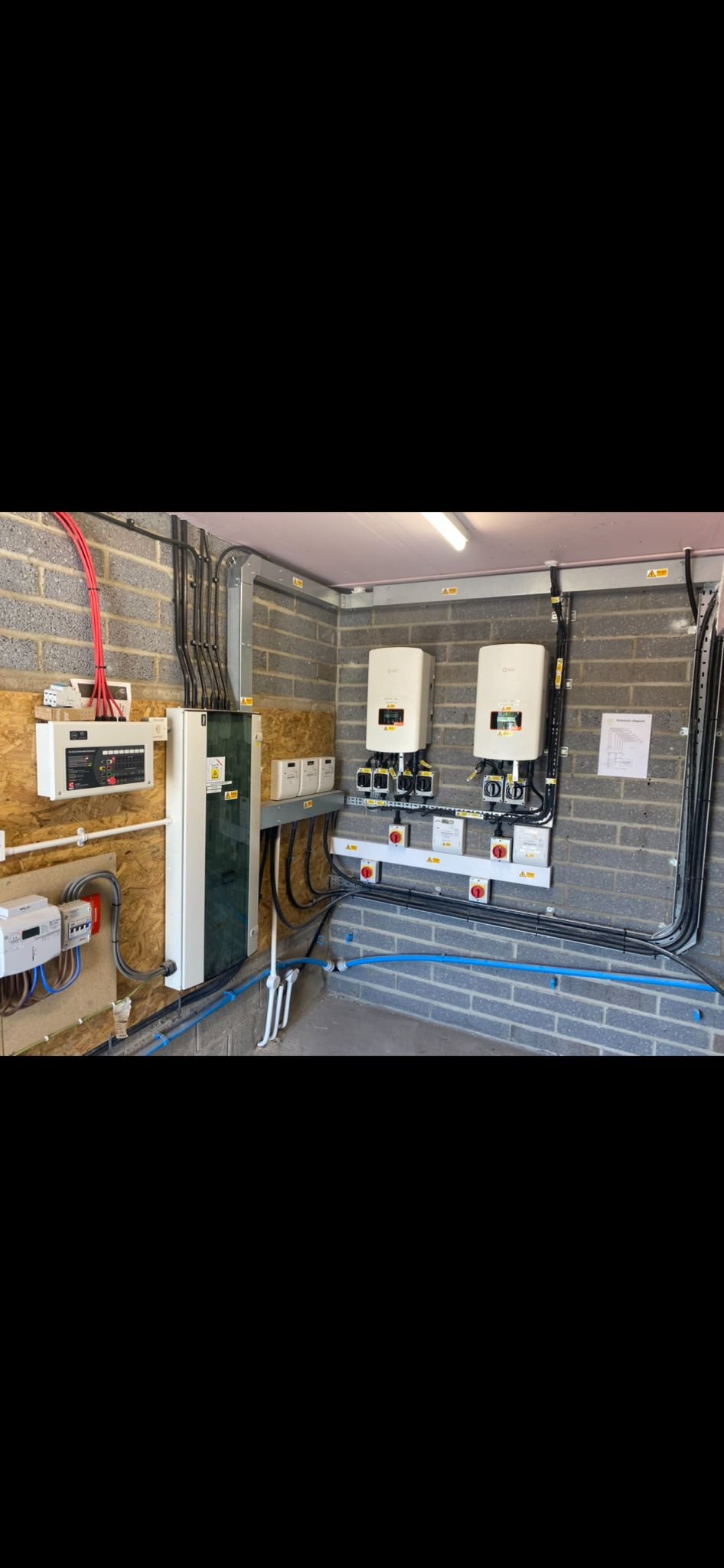 Electrical control panels, inverters, and wiring in a utility room with a brick wall.