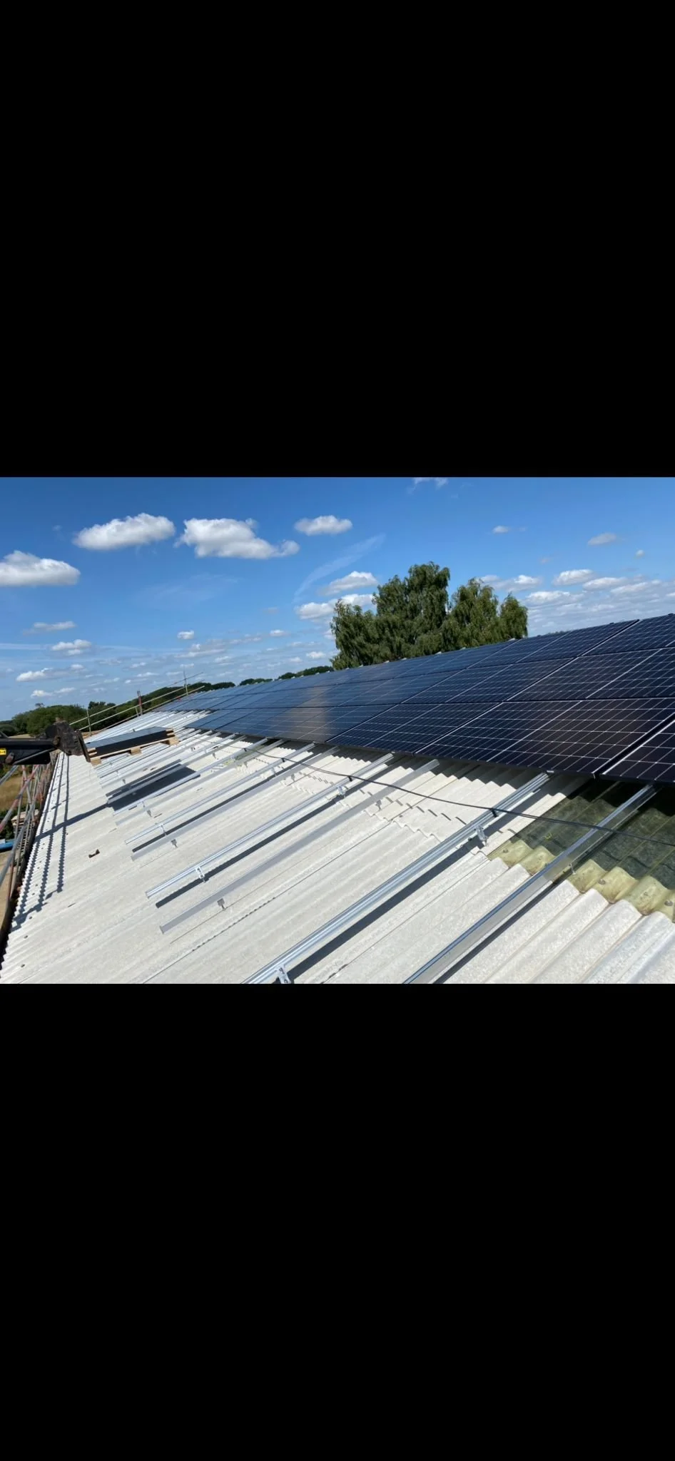 Solar panels installed on a corrugated metal roof under a partly cloudy blue sky.
