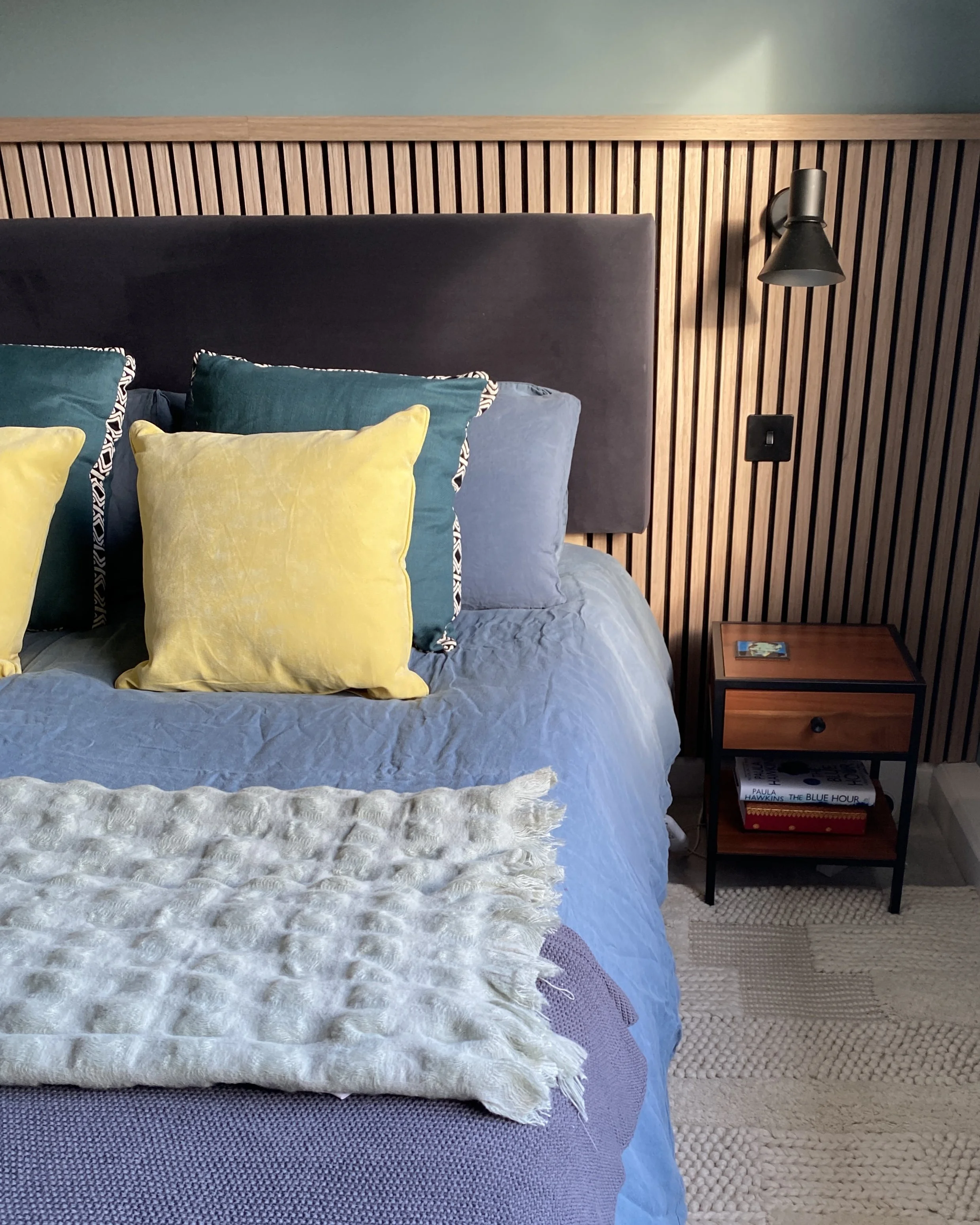 Image showing a bedroom styled with colourful cushions and with a contemporary half-panelled wall.
