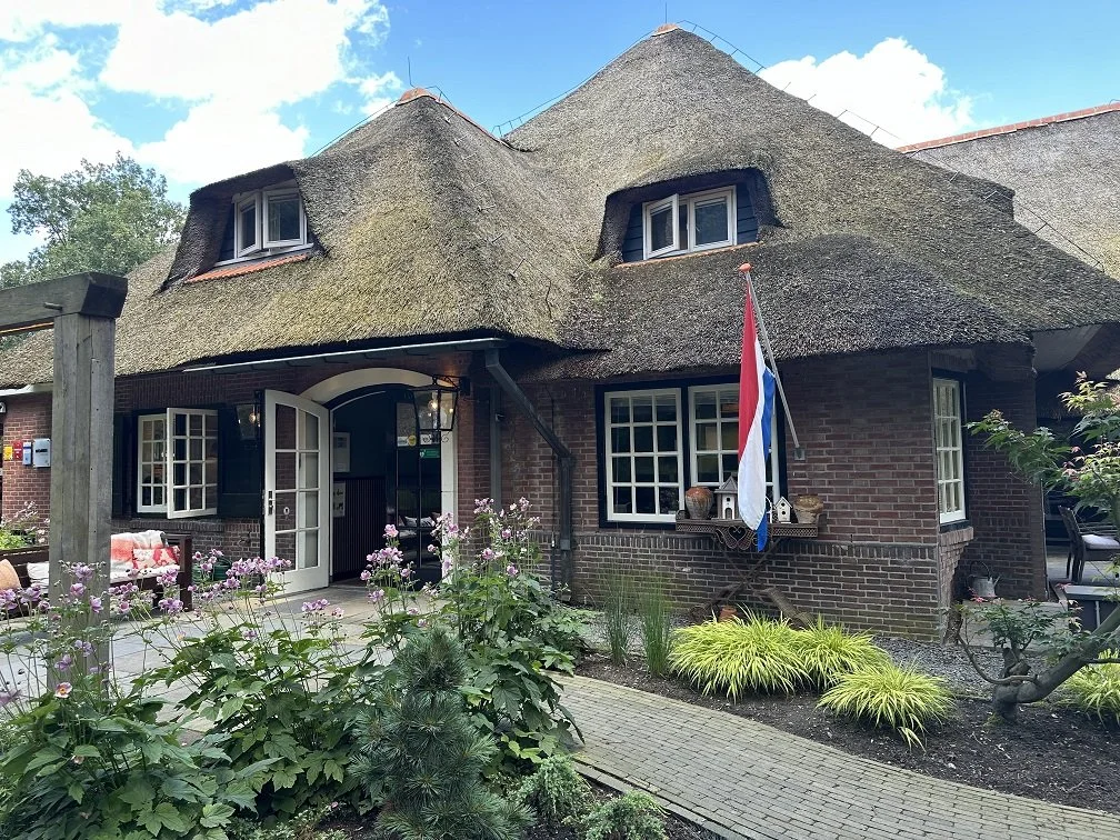 Gebouw Hoog Holten, entree met vlag en planten. Deur staat open.