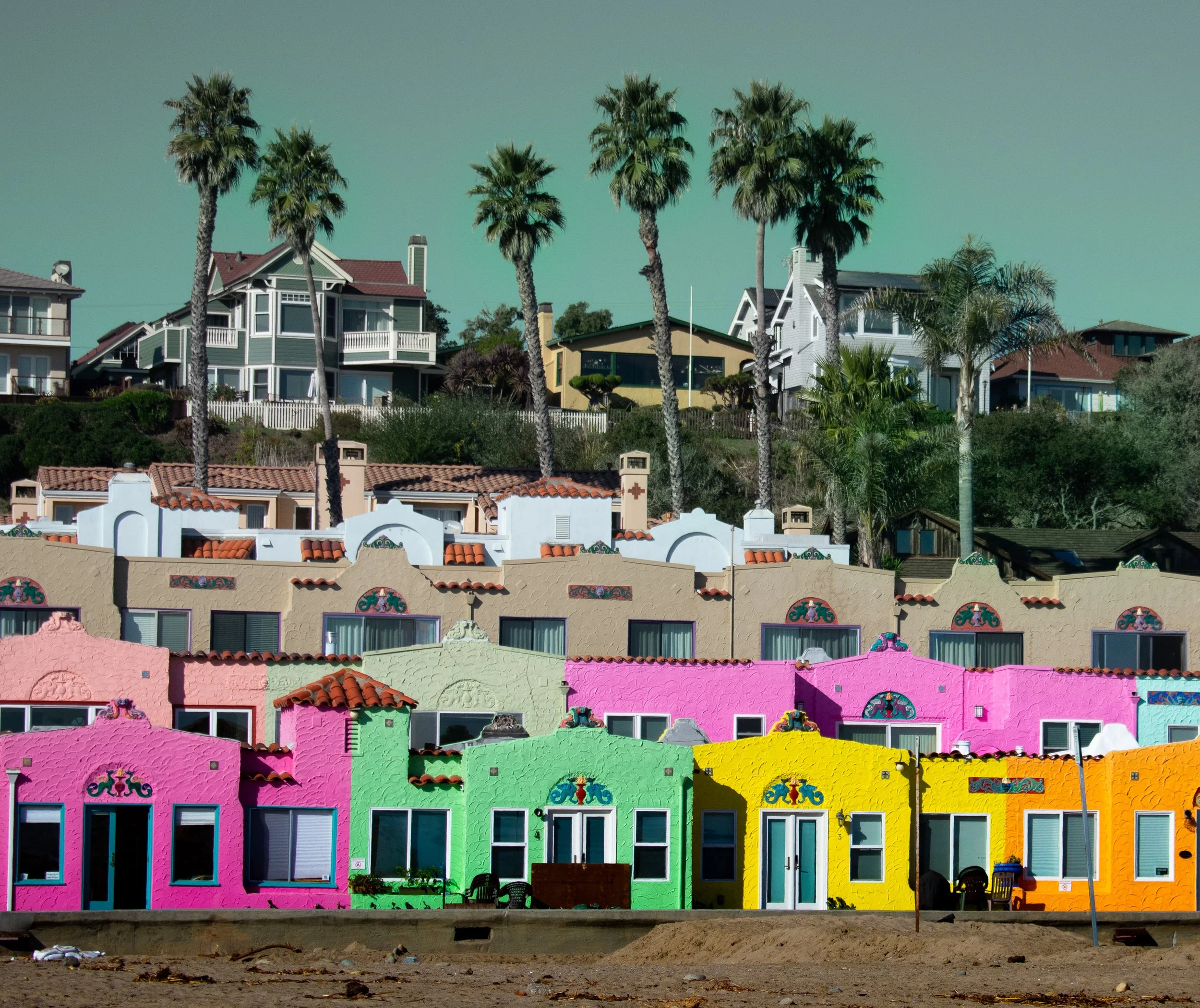 Colorful houses in Capitola, California, with palm trees on a hillside in the background.
