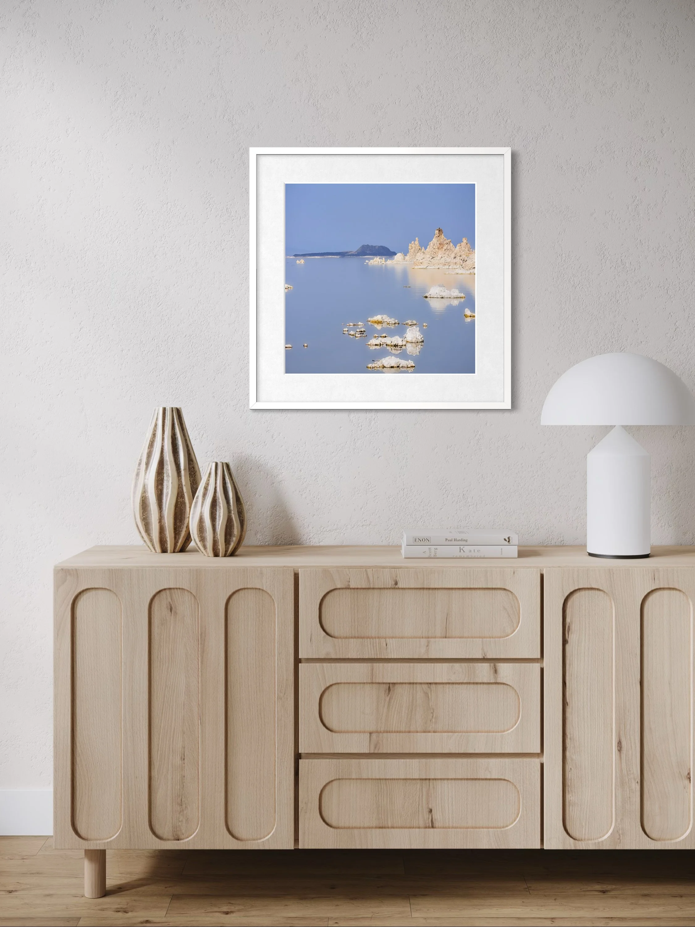 Decorative interior with wooden console table, framed landscape photograph of a lake and salt formations, white mushroom lamp, dried pampas grass, ceramic basket, small
