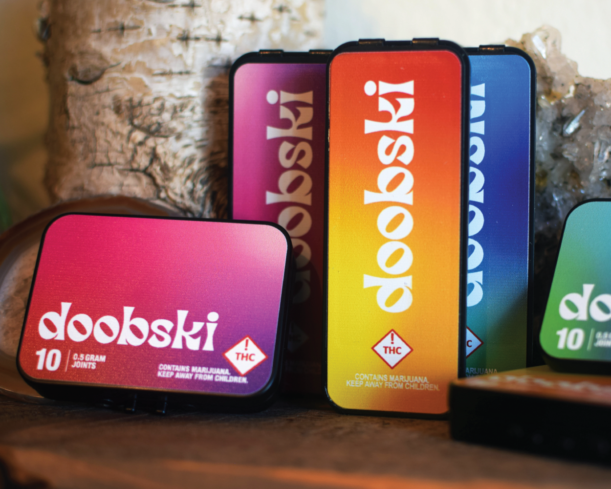 Multiple colorful packages of Doobski cannabis products, labeled with THC warnings, displayed on a wooden surface with a tree trunk in the background.