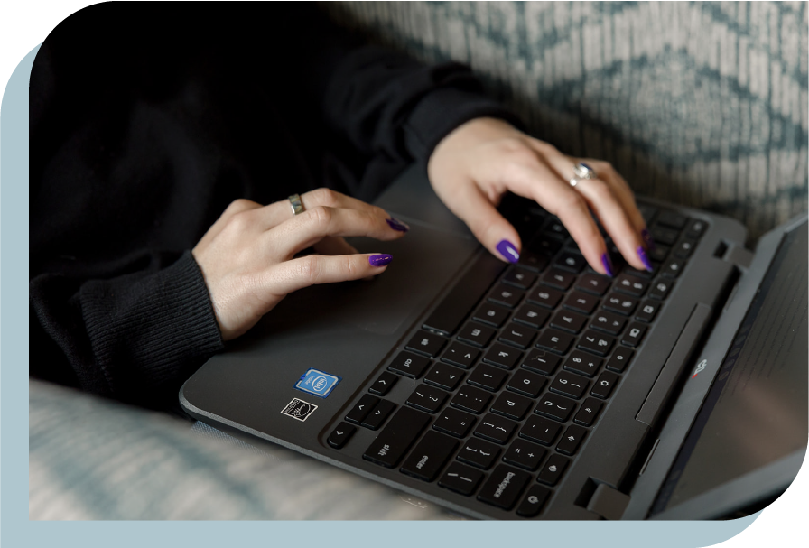 Close-up of person typing on a black laptop keyboard with purple painted nails, wearing rings, and a black long sleeve shirt.