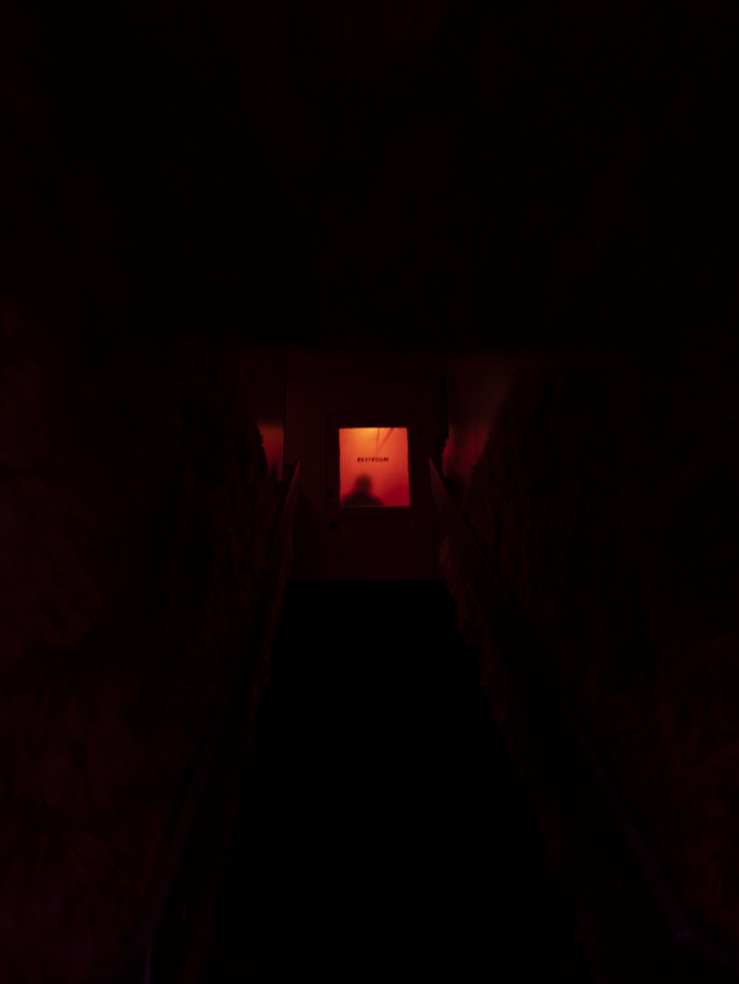 Dimly lit staircase with red lighting, leading to a partially illuminated door marked "restroom."