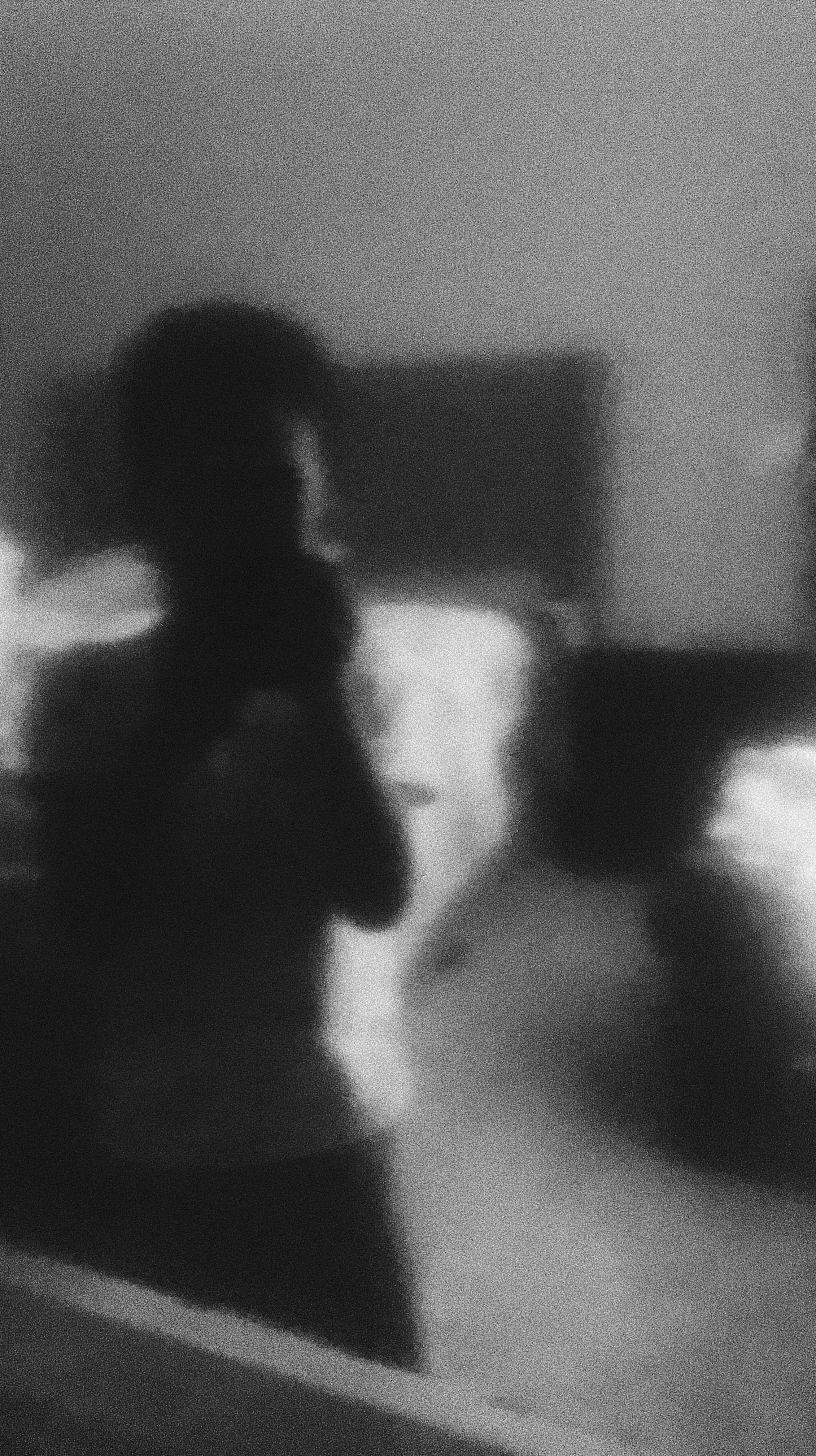Grainy black and white image of a person taking a mirror selfie in a dimly lit room.