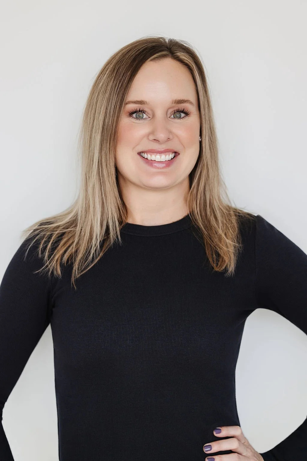 A woman with blonde hair, green eyes, wearing a black top, smiling against a white background.