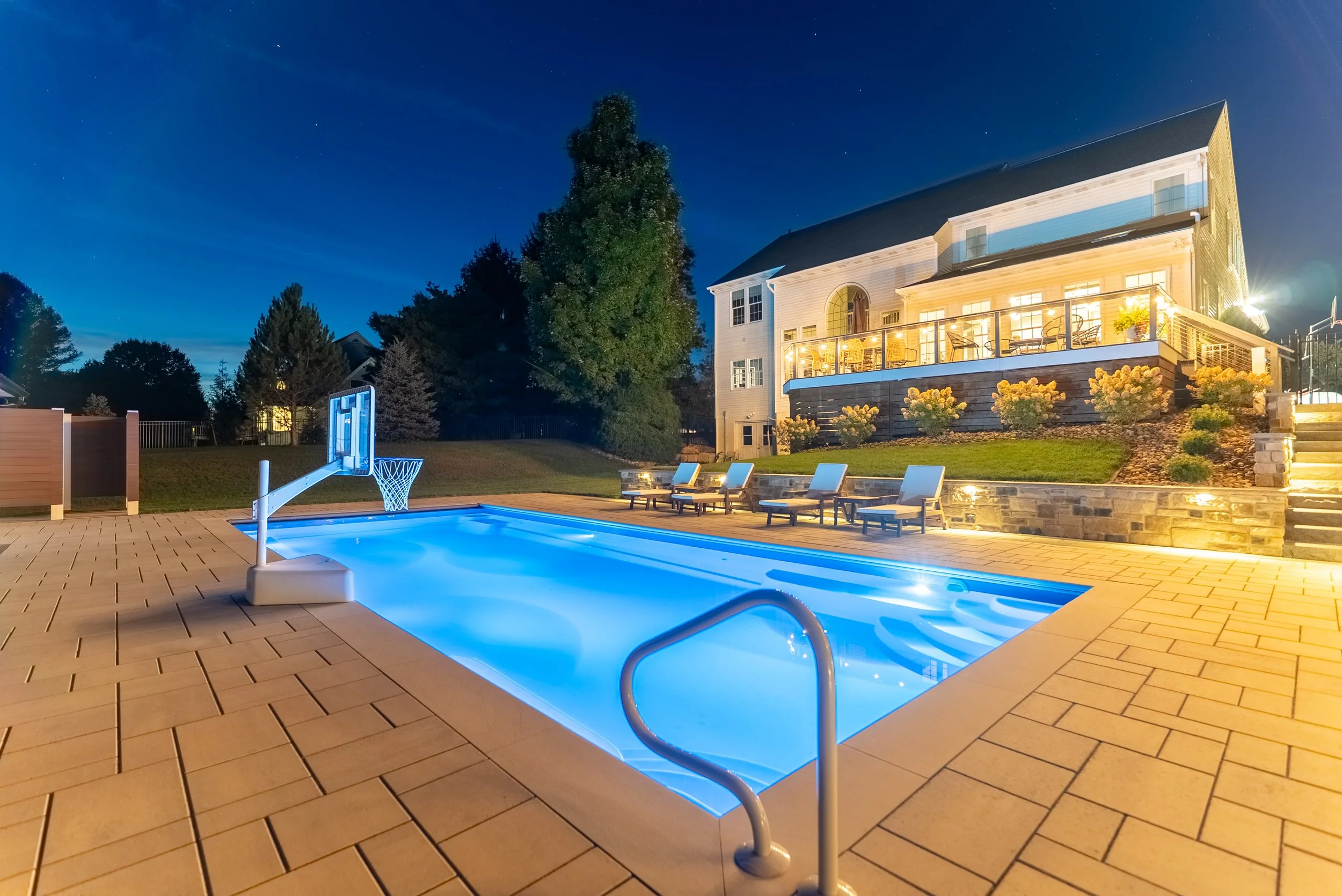 Blue-lit swimming pool beside a modern home at dusk.