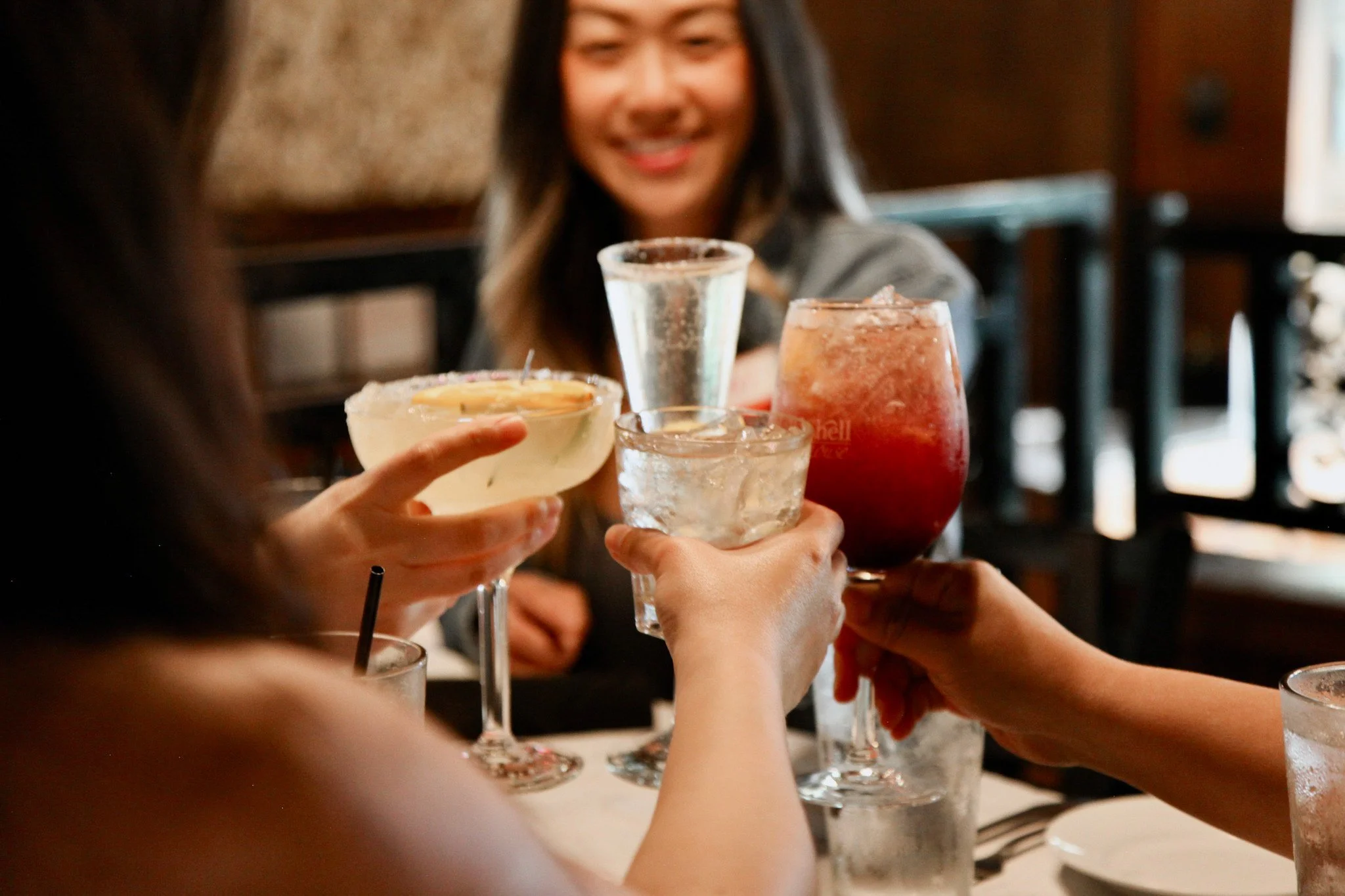 A group of middle aged women toasting with four colorful cocktails at Half Shell Oyster House