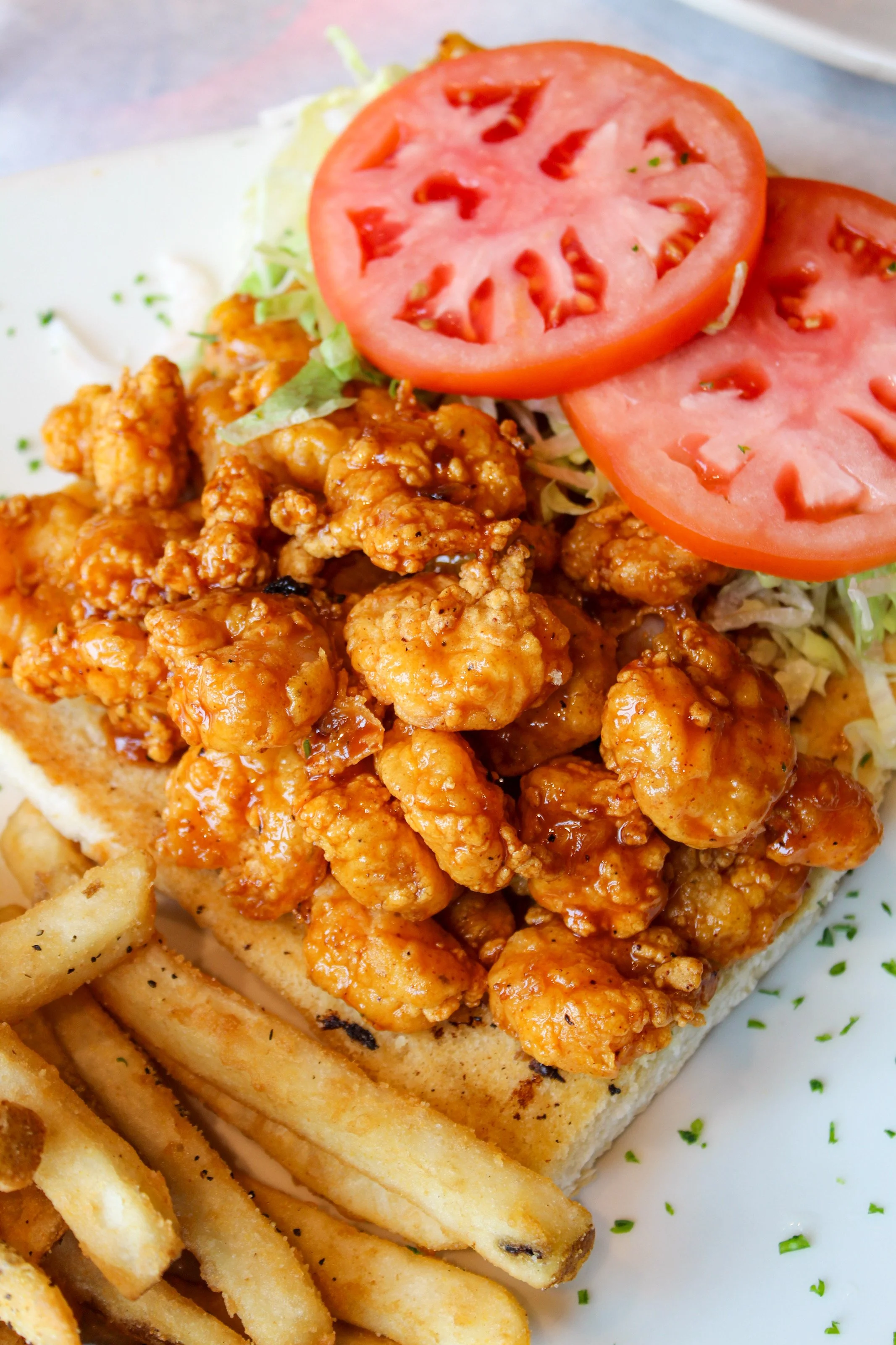 Fried chicken sandwich with lettuce and tomato on a bun, served with French fries.