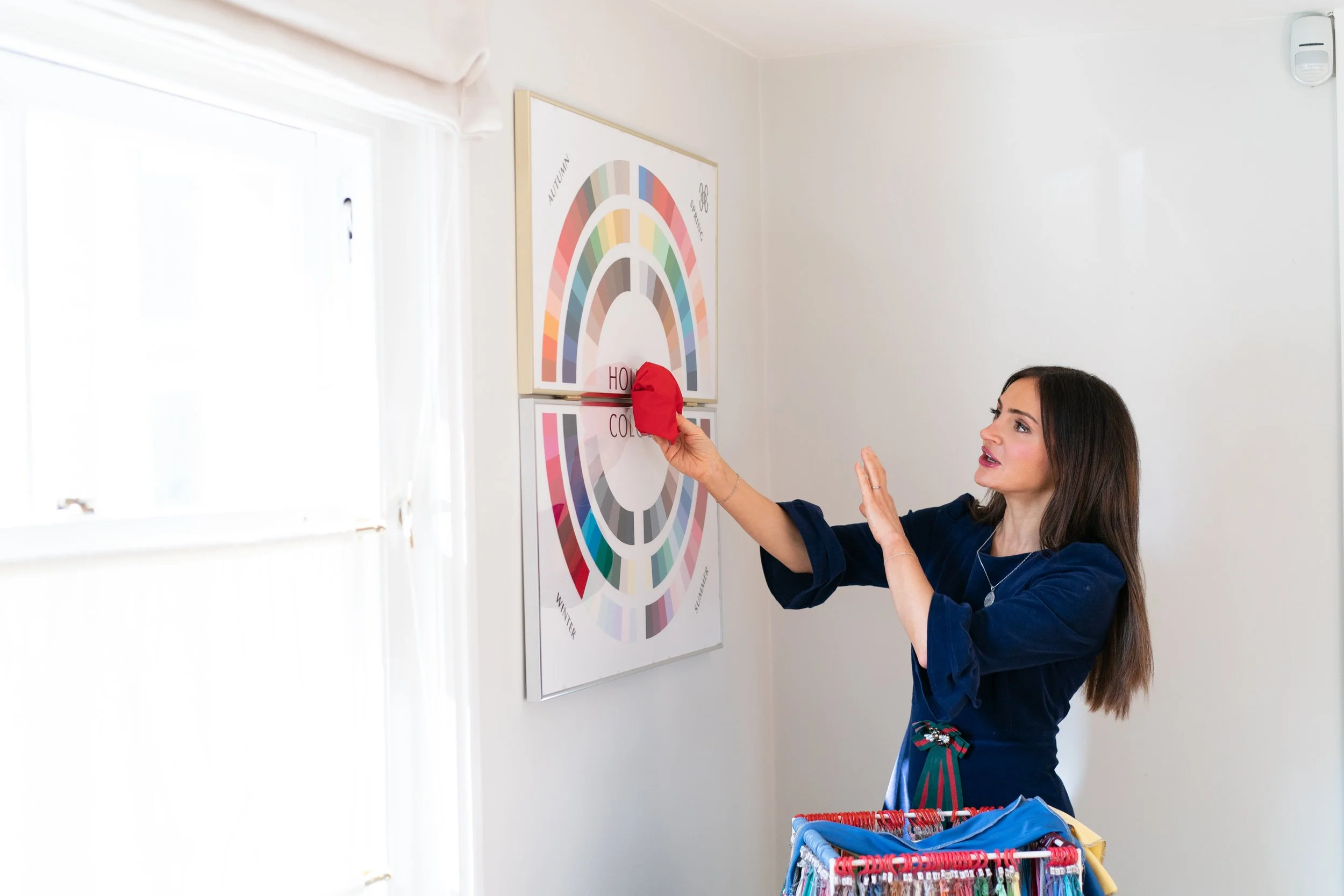 Woman with brunette hair holding a red colour swatch against a colour wheel on a white wall.