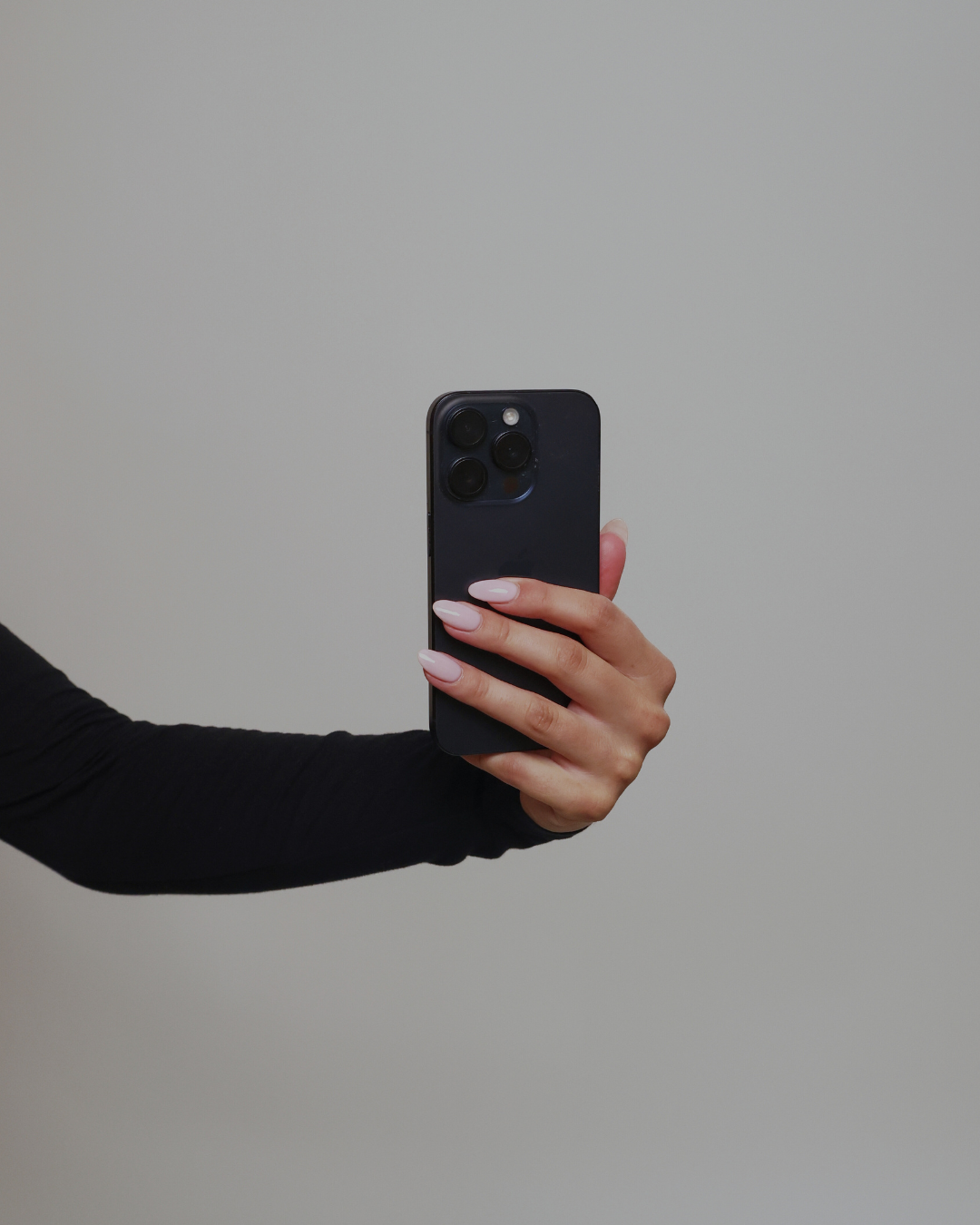 Close-up of a hand with pink nail varnish holding an iPhone up
