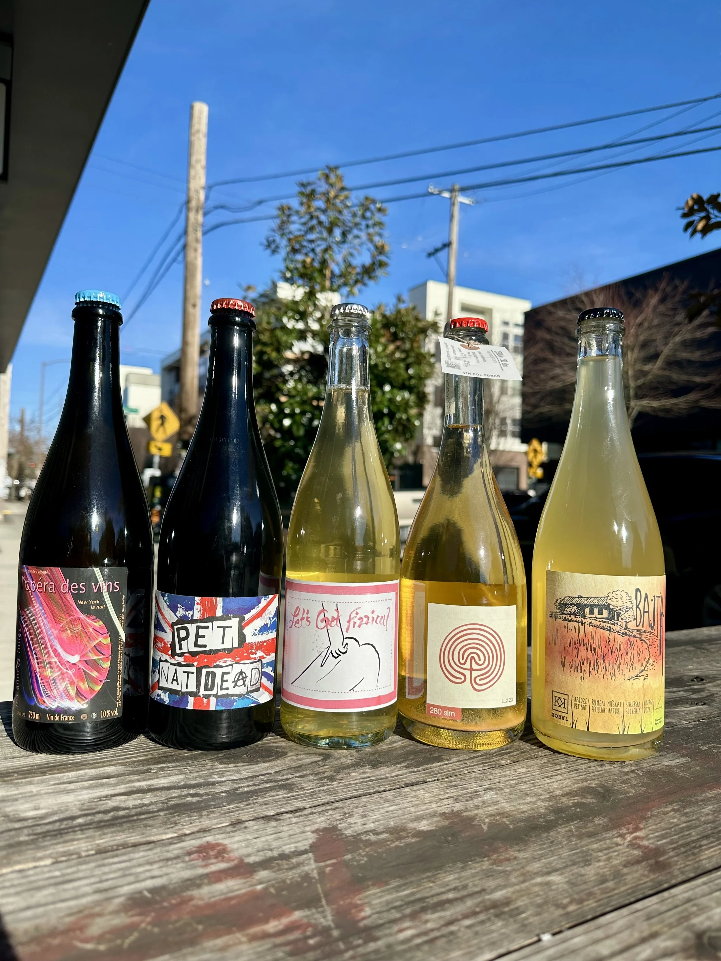 5 bottles of sparkling pet-nat wines on a picnic table outside