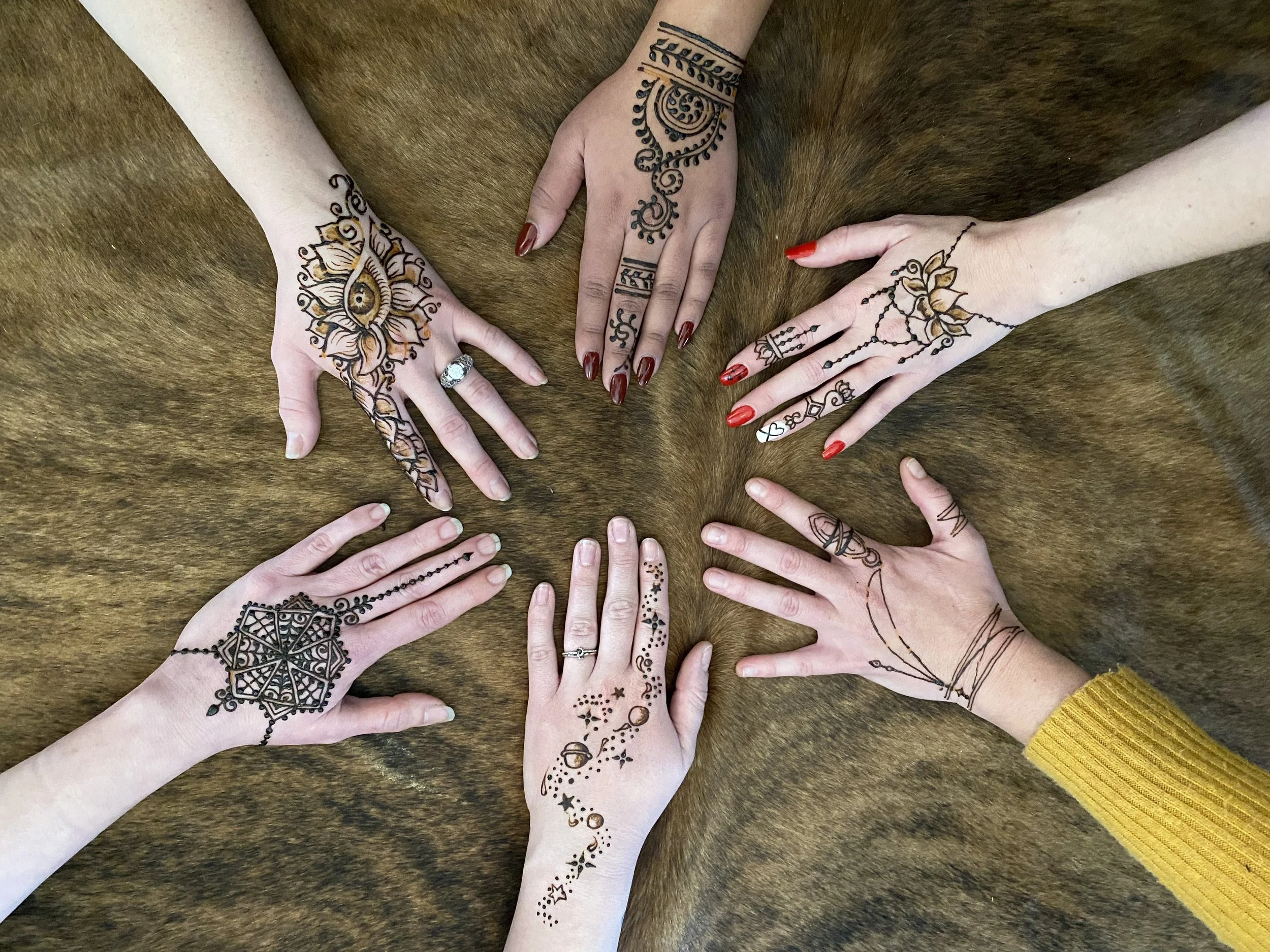 Five hands with intricate henna designs on a fur surface.