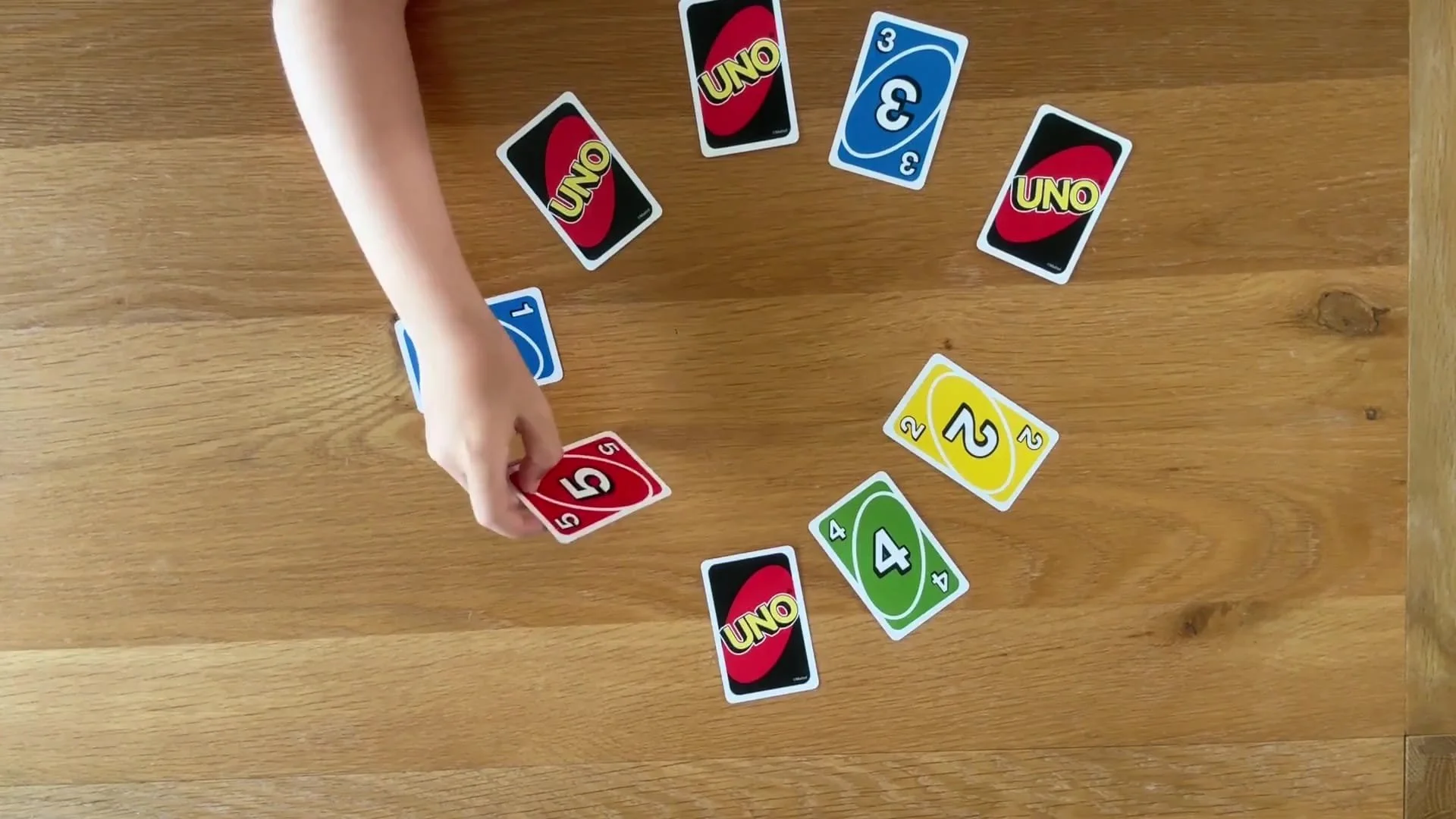 Uno cards are set up in a circle and a child is turning over the 4th card in the sequence.