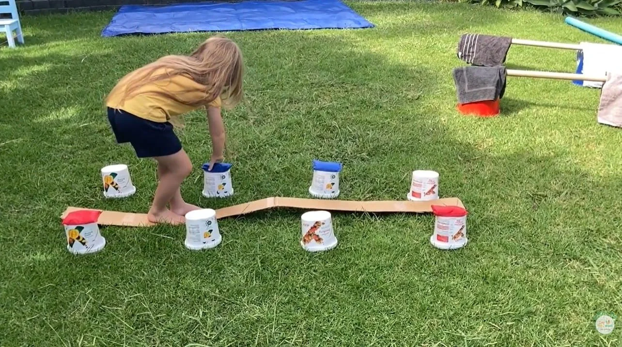 cardboard beam with child transferring bean bags from one side to the other