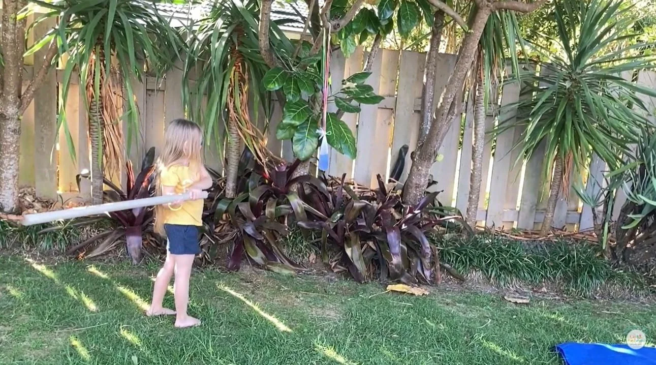 Child hitting a hanging toy with a cardboard tube