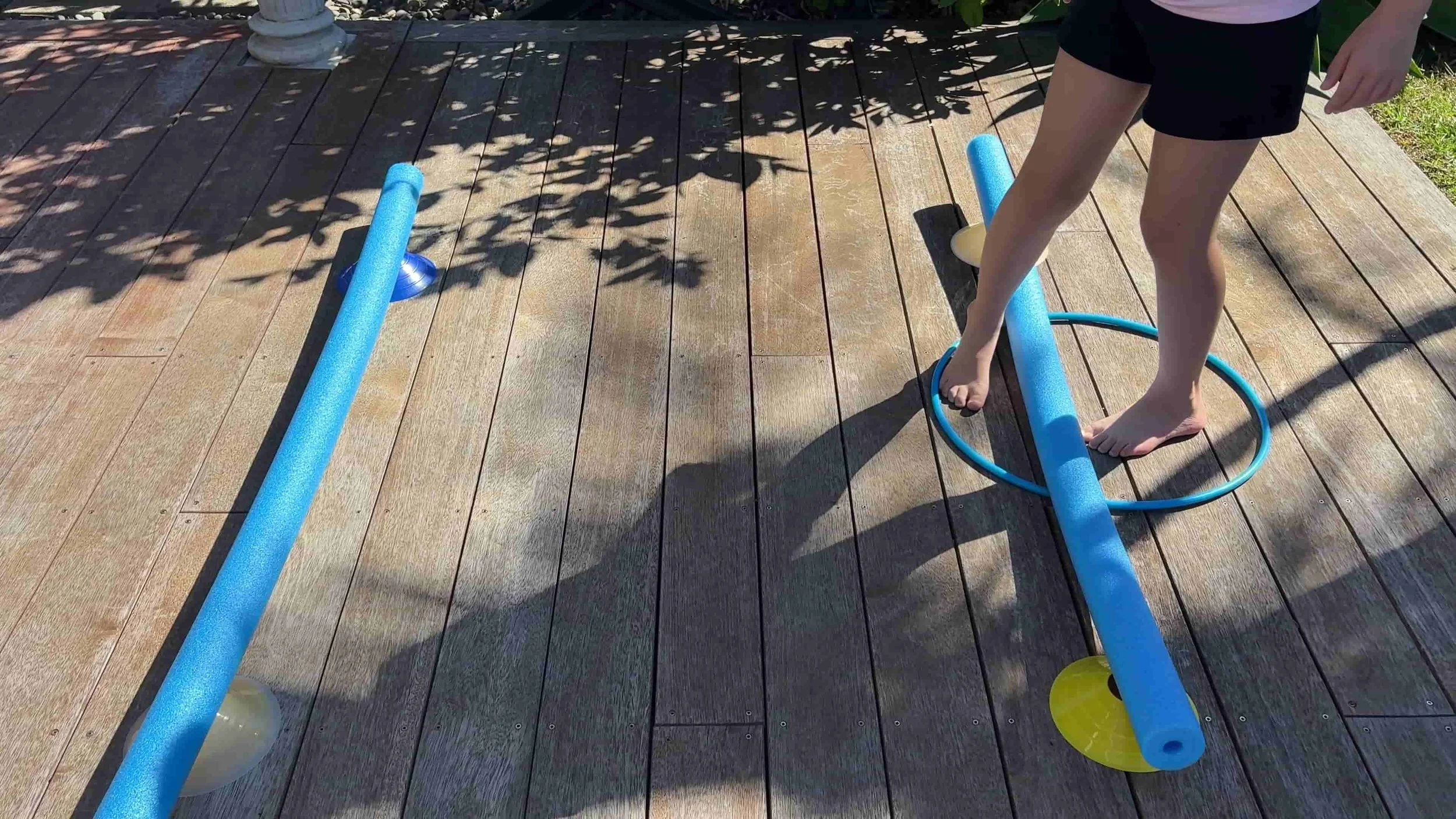 Child stepping over a pool noodle and moving a hula hoop along