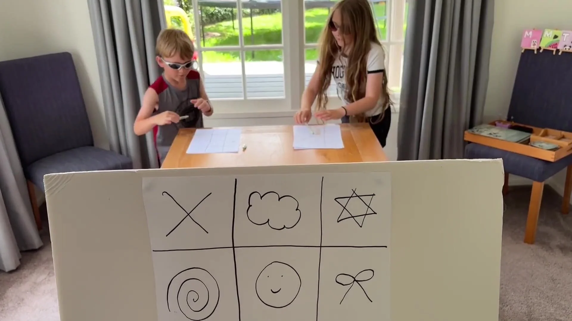 Grid attached to a board facing the camera and in the background, two players are filling in their own paper grid and preparing to run and check the big board.